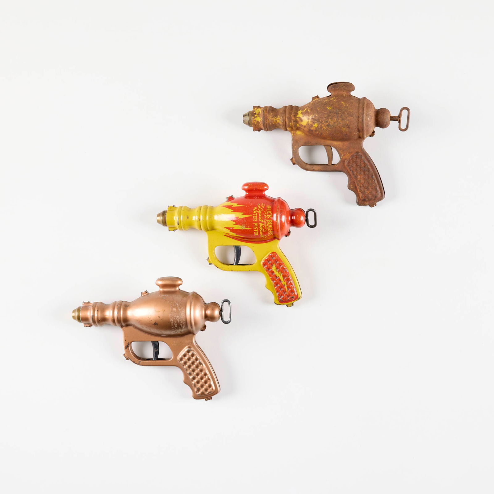 Three Daisy Buck Rogers Liquid Helium Water Pistols: Three Daisy Buck Rogers Liquid Helium Water Pistols transfer print and lacquered metal, zinc-plated steel 5.5 h x 7.5 w x 2.25 d in (14 x 19 x 6 cm) Manufacturer's mark to two examples. Condition Note
