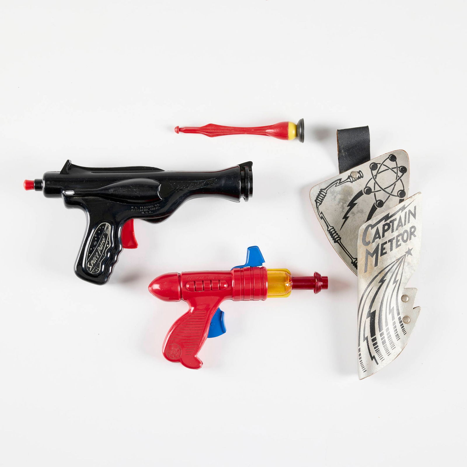 Two American Plastic Character Ray Guns: Two American Plastic Character Ray Guns molded plastic, screenprint on leather 5.5 h x 9.75 w x 2 d in (14 x 25 x 5 cm) 5.5 h x 7.625 w x 1.5 d in (14 x 19 x 4 cm) Includes a U.S. Plastics Co. Space P