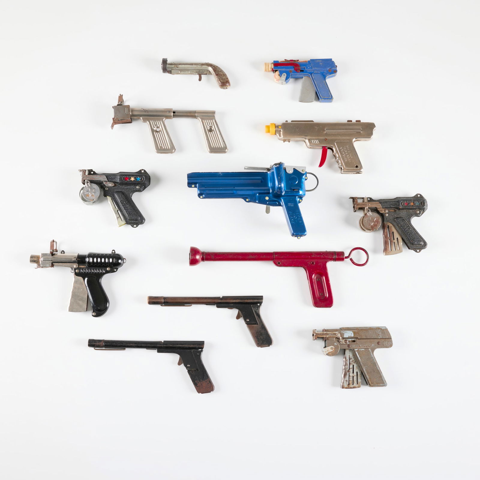 Twelve Early American Metal Click and Pop Paper Guns: Twelve Early American Metal Click and Pop Paper Guns enameled metal, zinc-plated steel, plastic largest: 4.5 h x 13 w x 1.5 d in (11 x 33 x 4 cm) smallest: 2.5 h x 5.5 w x 1.125 d in (6 x 14 x 3 cm) M