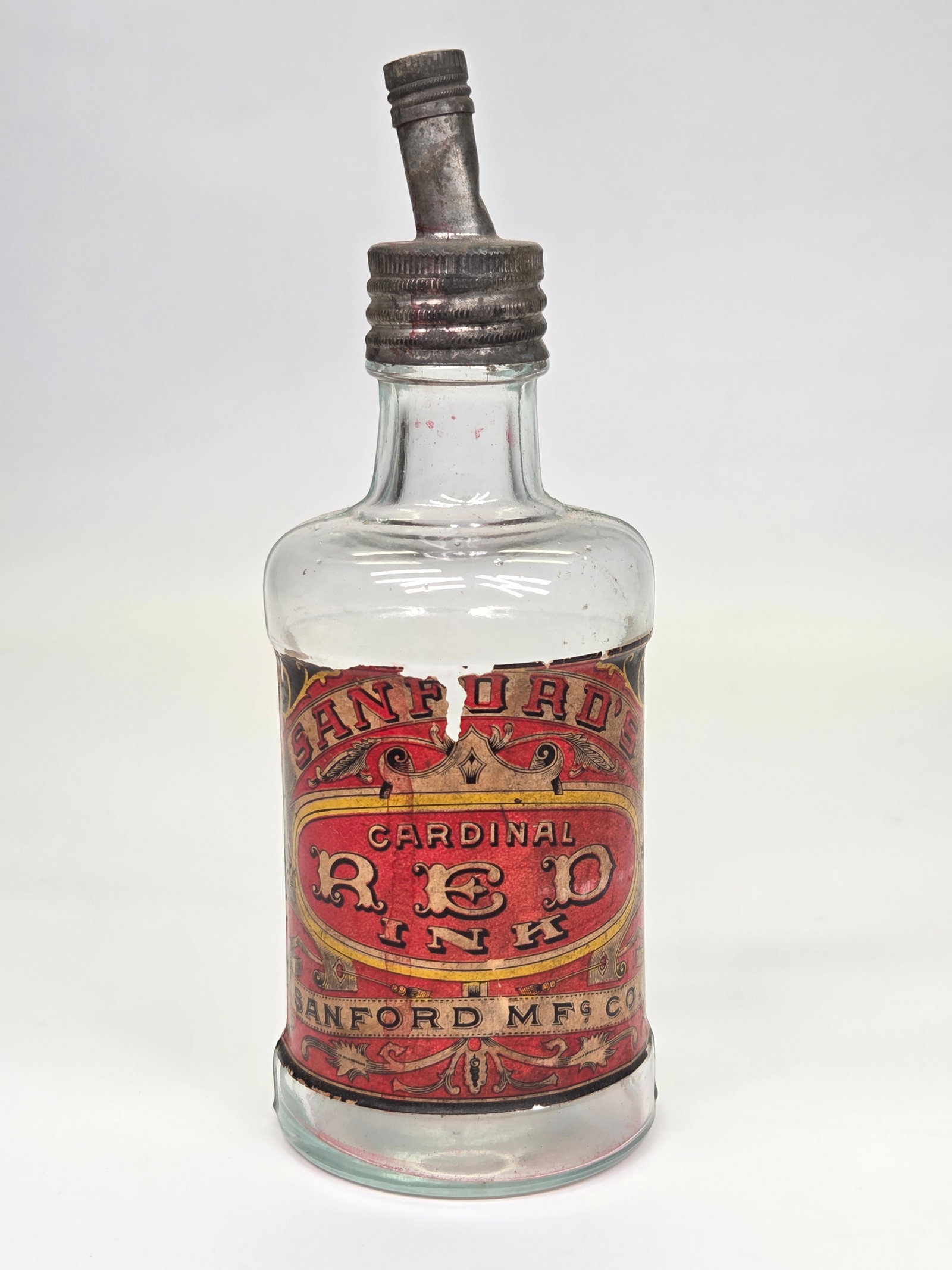 SANFORD MFG. CO. CARDINAL RED INK GLASS BOTTLE: BOTTLE REMAINS IN GOOD CONDITION WITH METAL SPOUT TOP. ORIGINAL LABEL SHOWING WEAR WITH SOME TEARS AND SOME STAINS.