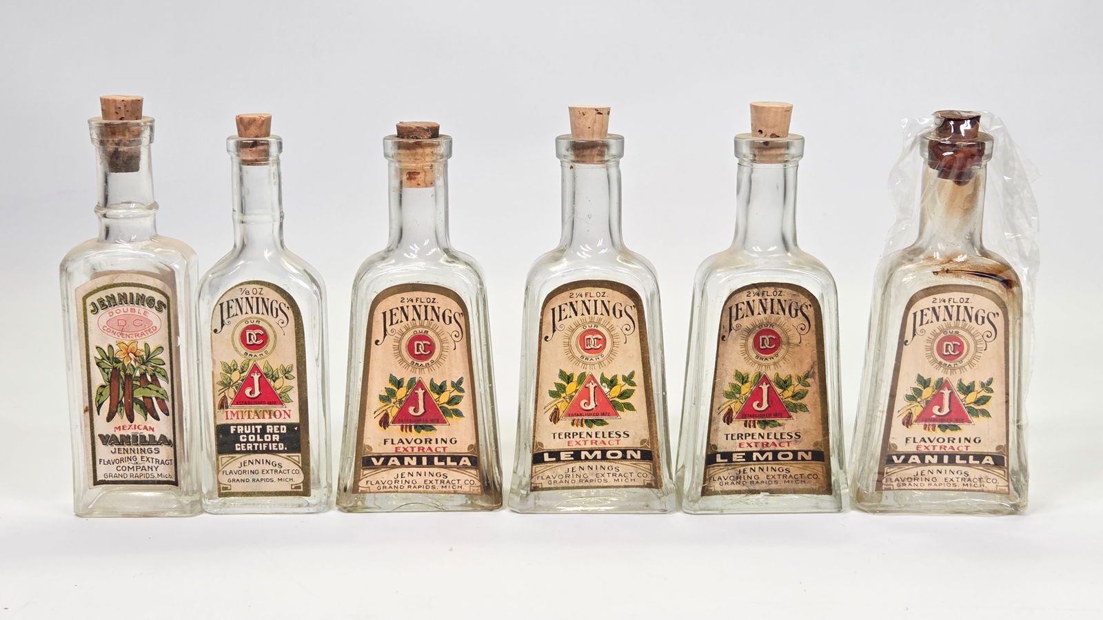 6) EARLY COUNTRY STORE JENNINGS EXTRACT GLASS BOTTLES: ALL REMAIN IN GOOD CONDITION WITH ORIGINAL LABELS. LABELS REMAIN NICE. ONE OF THE LEMON LABELS SHOWS STAINING. ALL EMPTY. A FEW CORKS ARE REPLACEMENTS.