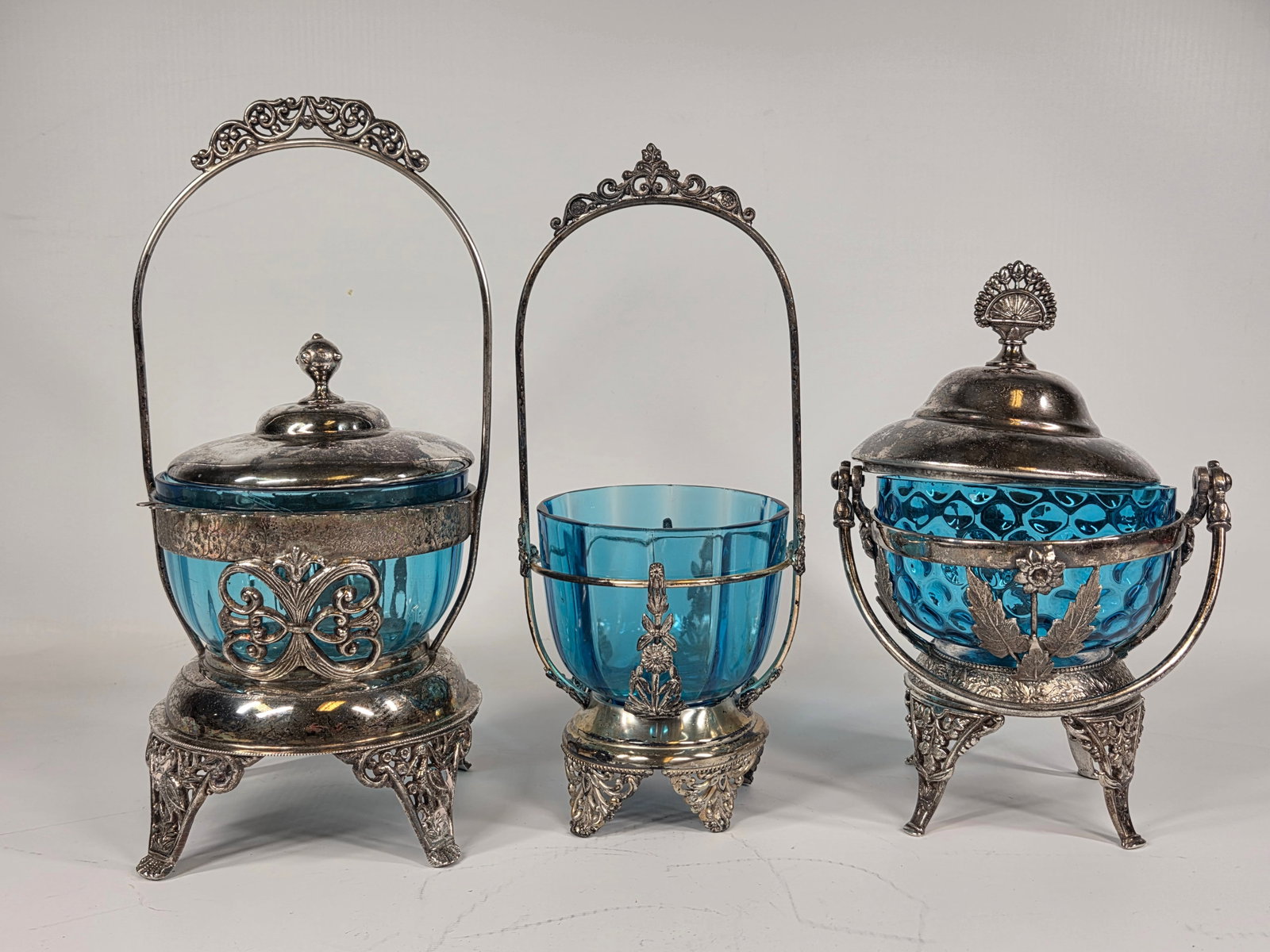 3) ANTIQUE VICTORIAN BLUE GLASS PICKLE CASTOR WITH SILVERPLATE STANDS: ALL REMAIN IN GOOD CONDITION, SHOWING SOME TYPICAL USAGE WEAR. EACH WITH A SMALL CHIP ALONG TOP EDGE. (1) LID IS OVERSIZED
