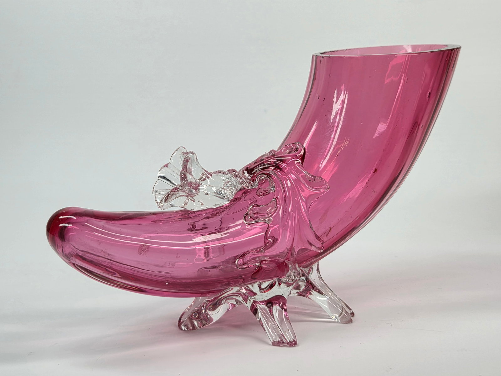 CRANBERRY ART GLASS CORNUCOPIA VASE W/ APPLIED FLOWER & FEET: REMAINS IN FAIR TO GOOD CONDITION, SHOWING SOME TYPICAL WEAR. A FEW SMALL MICRO CHIPS ALONG TOP EDGE. MULTIPLE CHIPS IN THE FEET.