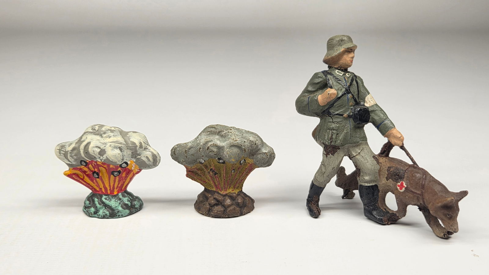 2) GERMAN ELASTOLIN COMPOSITION BOMBS & SOLDIER W/ DOG: BOTH BOMB EXPLOSIONS REMAIN IN GOOD CONDITION. SOLDIER HAS BROKEN HEAD WITH PART OF FEET MISSING.
