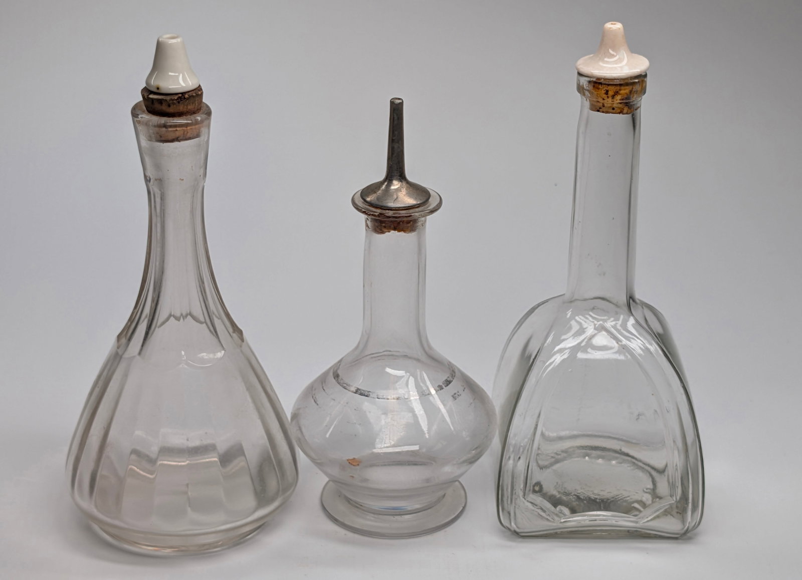 3) ASSORTED CLEAR GLASS BARBER'S TONIC COLOGNE BOTTLES W/ TOPS: REMAIN IN VERY GOOD CONDITION, SHOWING SOME LIGHT WEAR, DUST. NO CHIPS OR CRACKS.