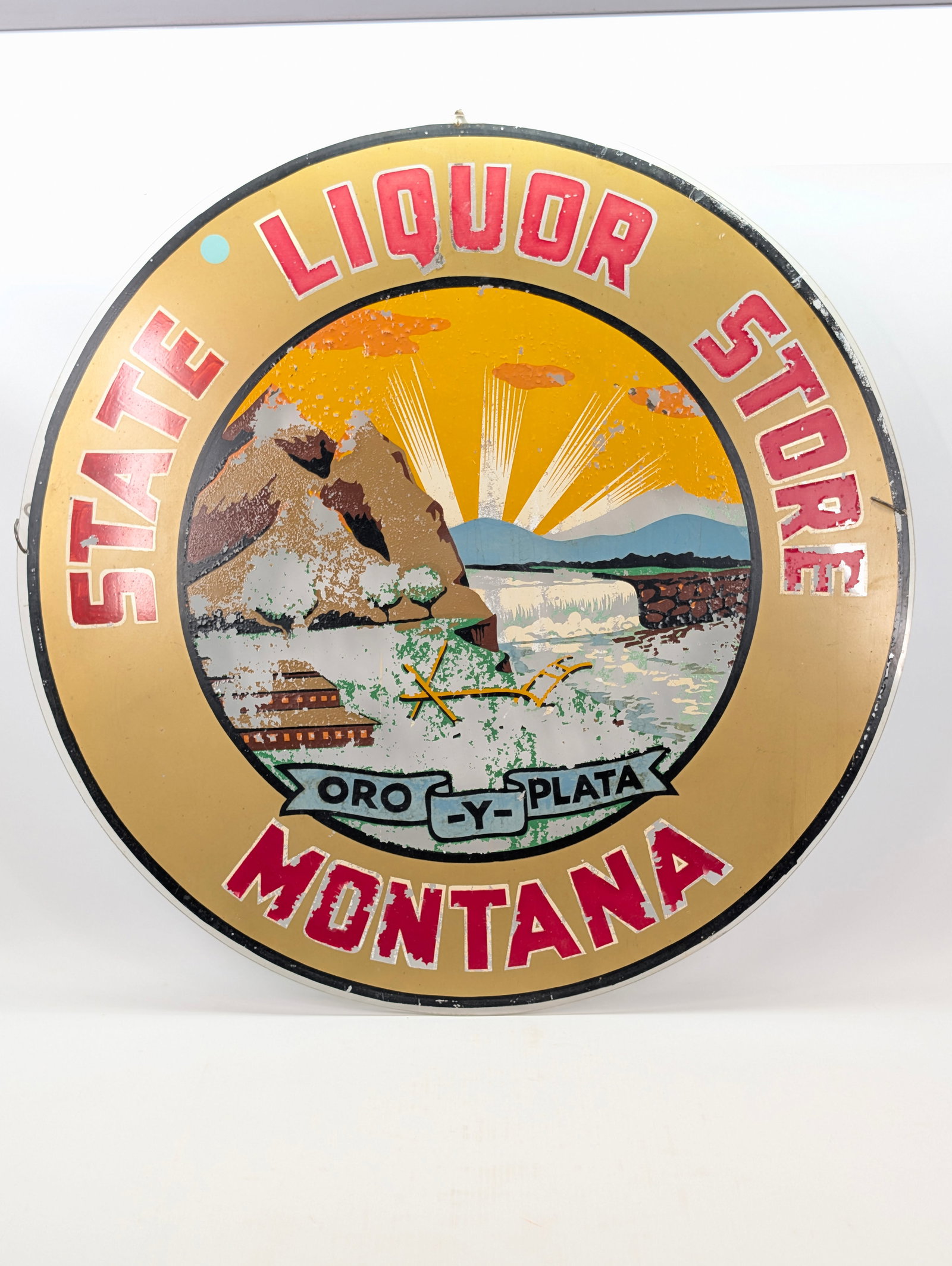 MONTANA STATE LIQUOR STORE REVERSE PAINTED GLASS SIGN: REMAINS IN FAIR TO GOOD CONDITION, SHOWING SOME TYPICAL USAGE WEAR. NO CHIPS OR CRACKS. SHOWS PAINT LOSS TO CENTER IMAGE.