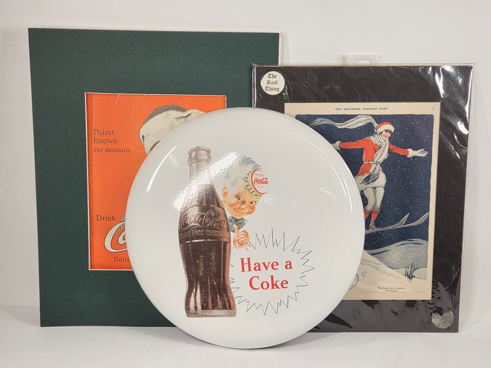 REPRODUCTION COCA COLA BUTTON & 2) ADVERTISEMENTS: BUTTON REMAINS IN GOOD CONDITION, SHOWING LIGHT WEAR. ADVERTISEMENTS SHOWING SOME LIGHT WEAR.