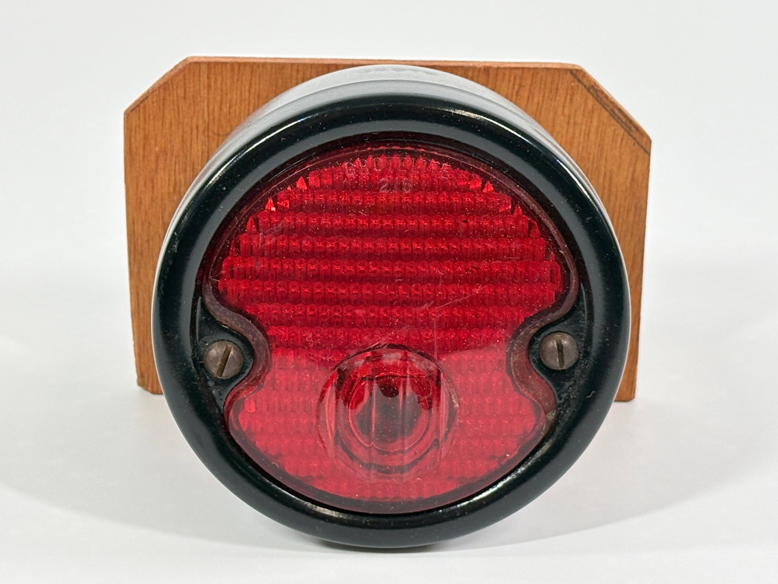 RED CLASS AUTOMOBILE LIGHT: REMAINS IN GOOD CONDITION, SHOWING LIGHT WEAR. MOUNTED ON BOARD.