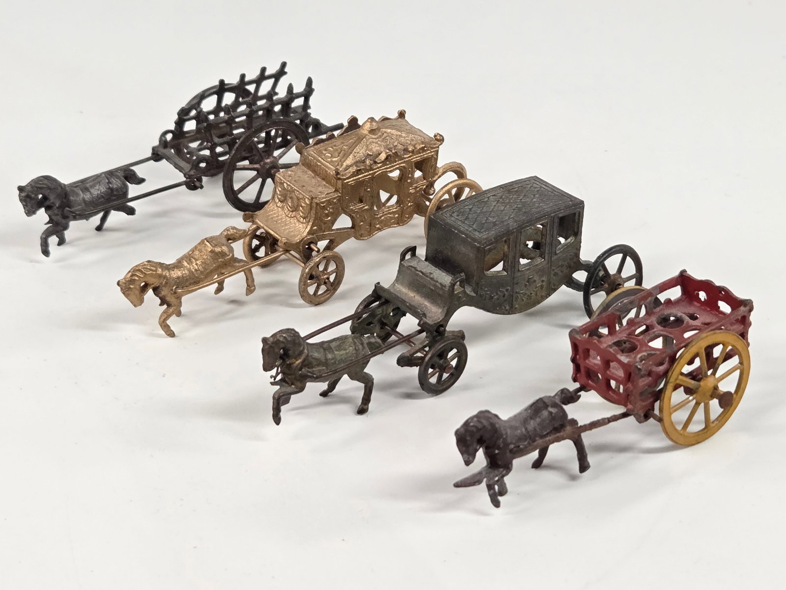 4) MINIATURE CRACKER JACK STYLE HORSE DRAWN CARS: ALL REMAIN IN FAIR TO GOOD CONDITION, SHOWING SOME TYPICAL WEAR. SOME BENDS NOTICED.