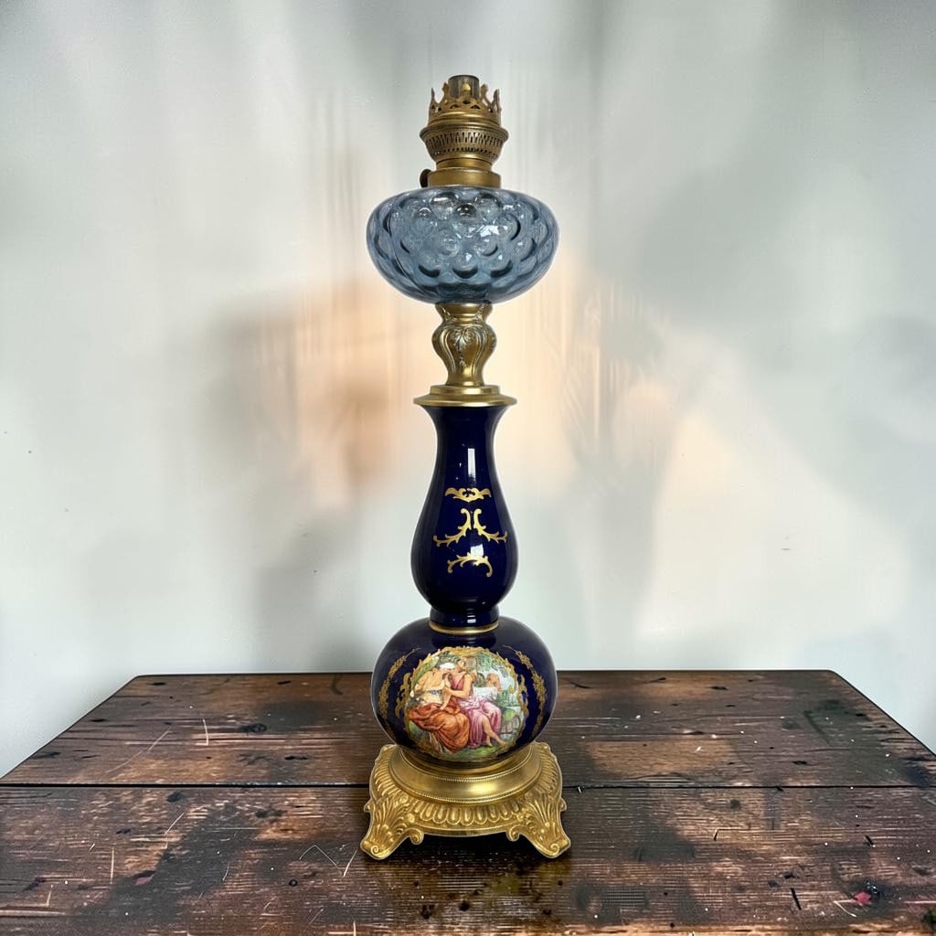 Antique French Sevres Style Cobalt Blue Porcelain Oil Lamp with Gilt Bronze Mounts: This elegant antique French Sevres style porcelain oil lamp features a richly decorated cobalt blue porcelain body adorned with hand-painted romantic figural scenes and ornate gilt detailing. Crafted 