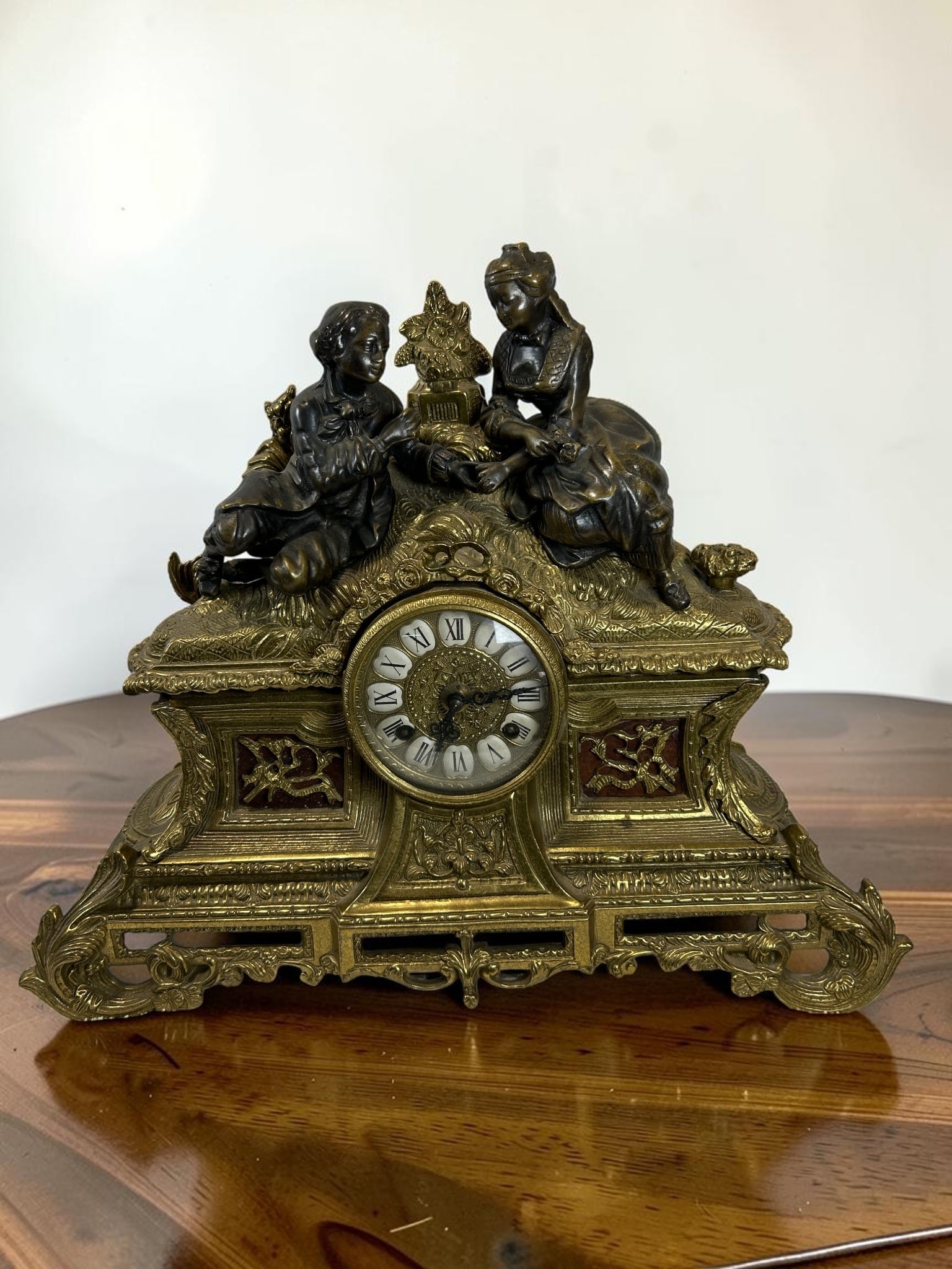 Antique French Louis XV Style Franz Hermle & Sohn Gilt Metal Mantel Clock with Bronze Figures: This charming antique French Louis XV style mantel clock features an elaborate gilt metal case adorned with richly cast Rococo-inspired ornamentation and beautifully detailed bronze patinated female a