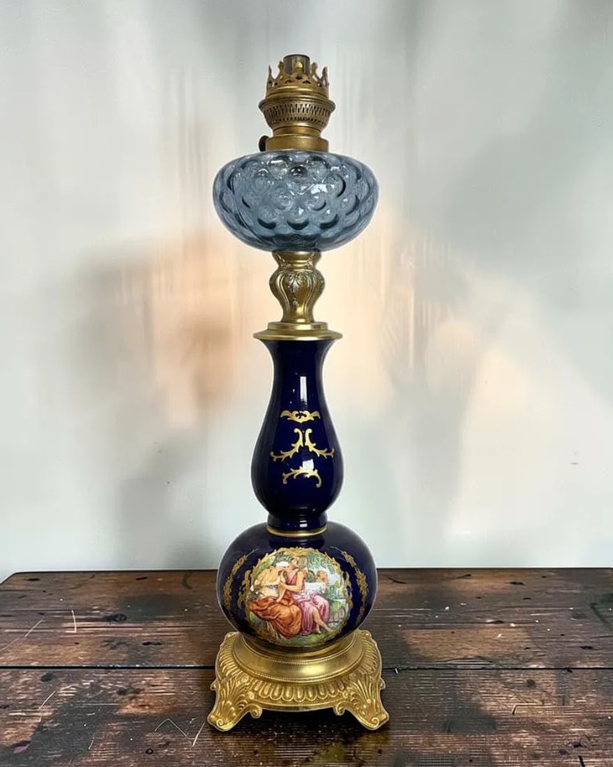 French Sevres Style Cobalt Blue Porcelain Oil Lamp with Gilt Bronze Mounts: This elegant French Sevres style porcelain oil lamp features a richly decorated cobalt blue porcelain body adorned with hand-painted romantic figural scenes and ornate gilt detailing. Crafted from fin