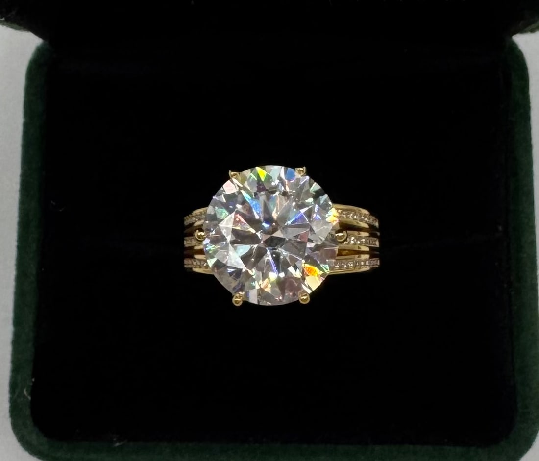 Impressive 10.00ct Round Brilliant Cut Moissanite Ring - 18k Gold over Silver: Center Stone: 10.00 Carat Round Brilliant Cut Moissanite.• Metal: 18k Gold Plating over Solid .925 Sterling Silver.• Design: Modern triple-shank band set with accent stones for maximum brill