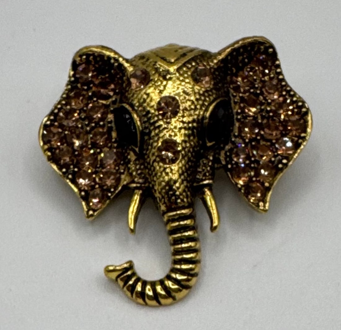 Ornate Gold-Tone Elephant Head Brooch with Champagne Rhinestone Pave Ears: Design: A detailed, textured elephant head casting featuring an upturned trunk (traditionally a symbol of good luck).• Accents: The ears and forehead are intricately set with shimmering champagne