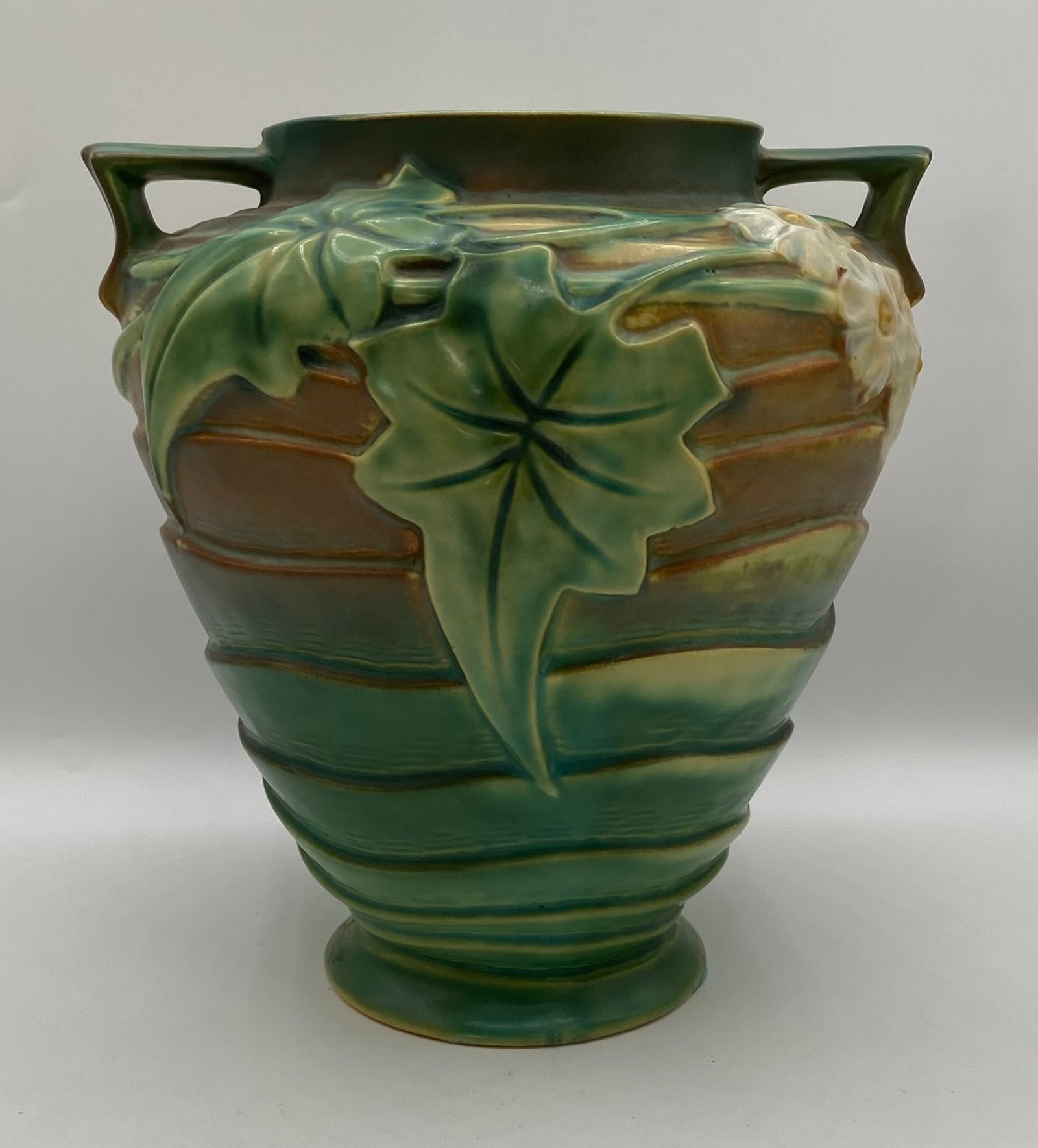 Roseville Pottery Luffa Water Lily Green Double-Handled Vase - 9": An attractive Roseville Pottery double-handled vase in the "Water Lily" pattern (introduced circa 1943), featuring relief-molded green lily pads and white blossoms against a gradient ribbed body of de