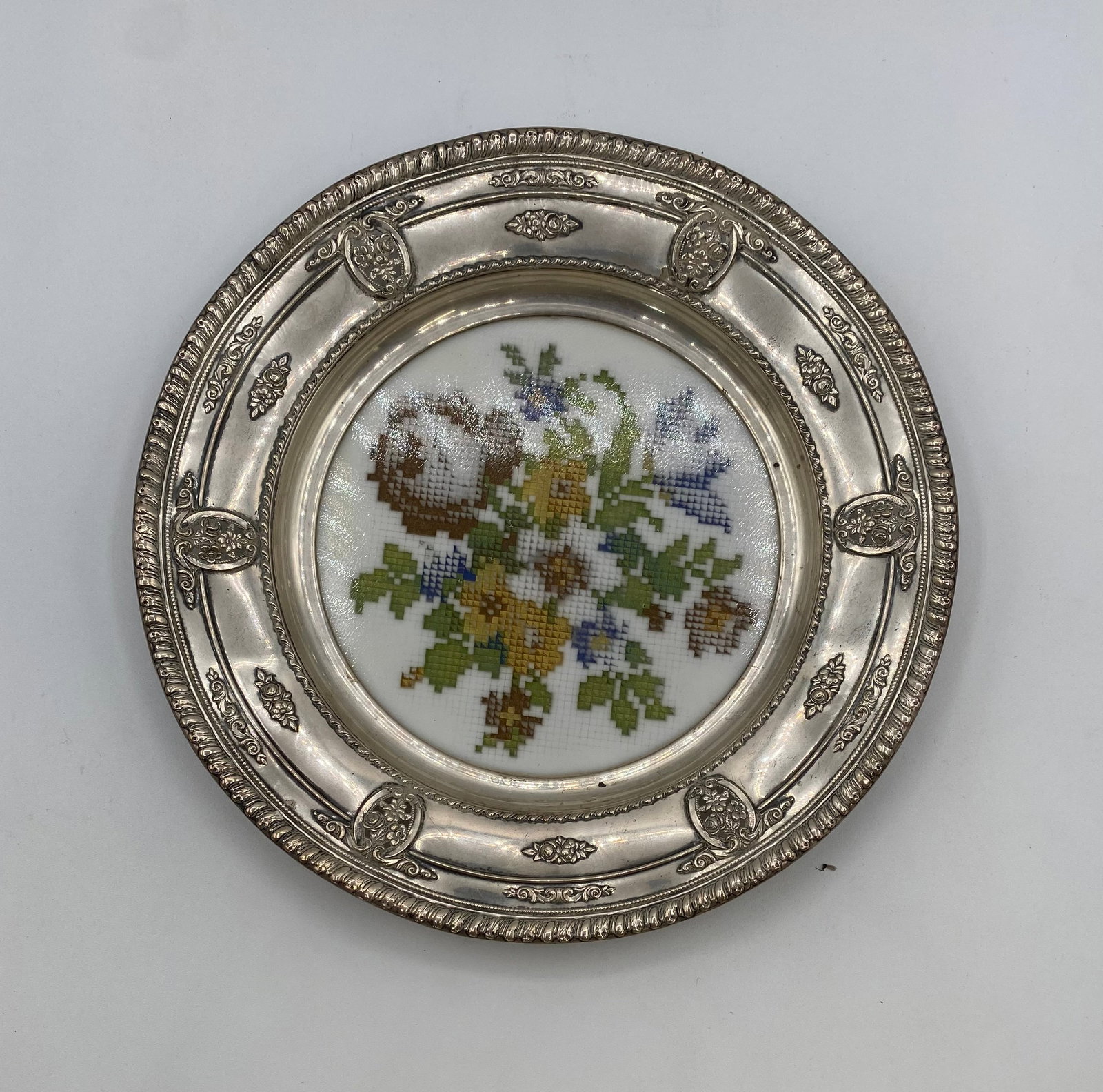 Vintage Mid-Century Silver Plate & Glass Needlepoint Tray / Trivet, 8": Up for auction is a vintage round silver-plated vanity tray / trivet featuring an ornate embossed rim with scroll and floral accents. The inset center displays a hand-worked floral needlepoint / cross