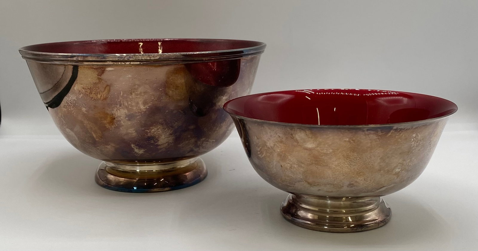 Pair of Towle & Reed & Barton Silver Plate & Ruby Red Enamel Bowls: Up for auction is a pair of vintage silver-plated nesting / footed bowls with rich ruby red enamel interiors. The larger bowl is produced by Towle Silversmiths, featuring a deep crimson enamel interio