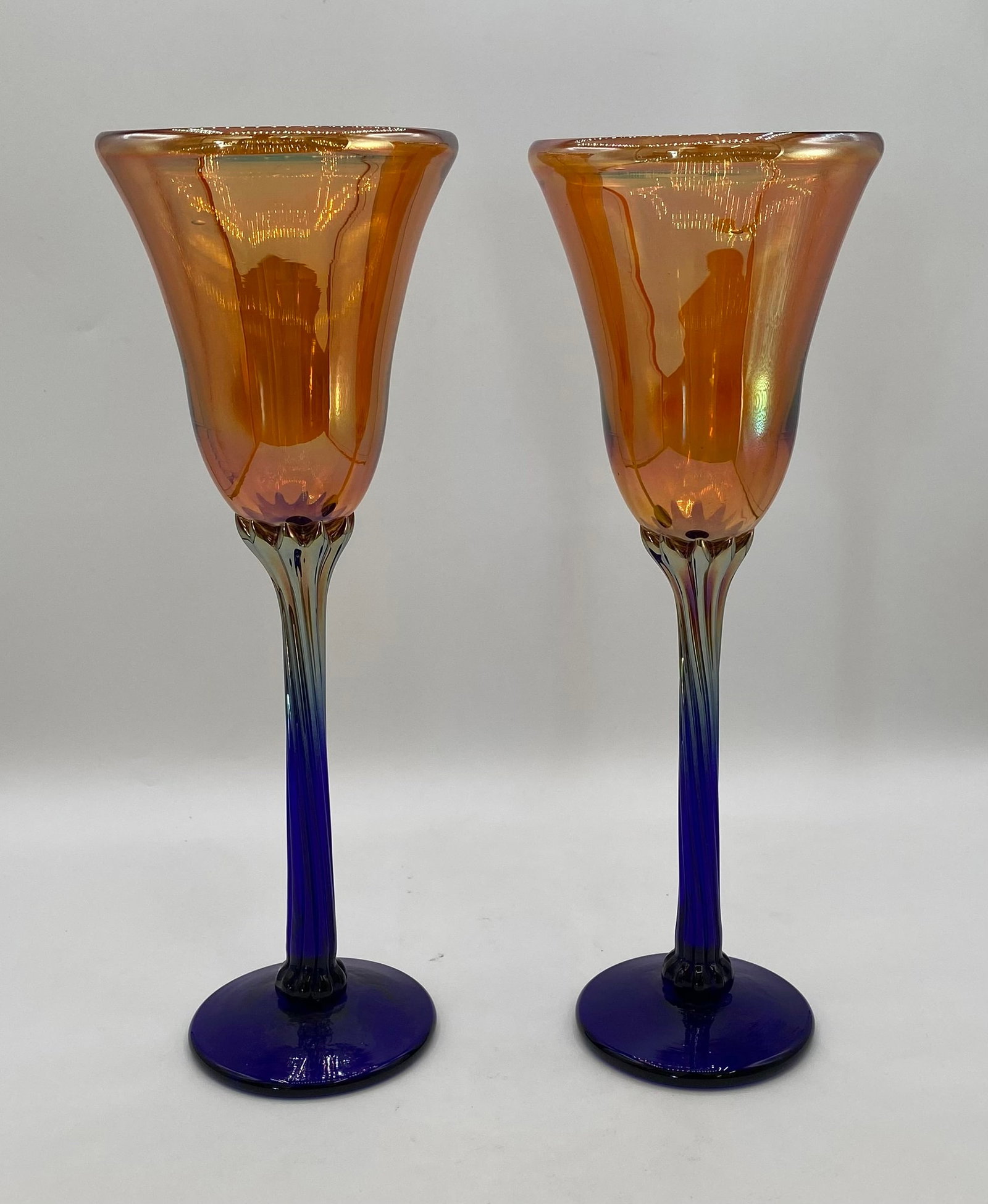 Pair of Hand-Blown Studio Art Glass Iridescent Amber & Cobalt Wine Goblets: Up for auction is a striking pair of hand-blown studio art glass wine goblets. Each goblet features an iridescent amber-gold lustre tulip bowl with subtle pulled trailing accents, elevated on a slende