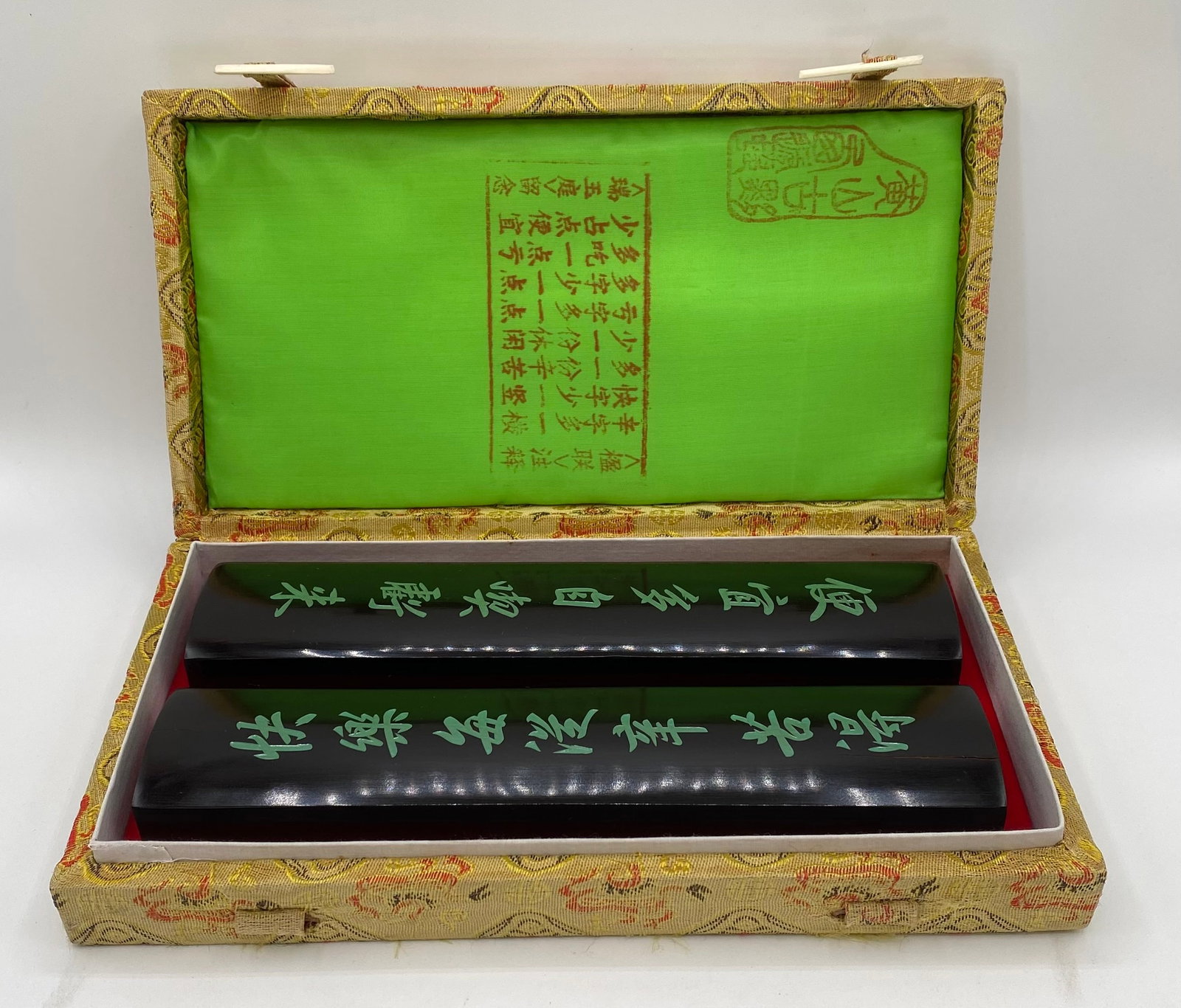 Vintage Chinese Carved Calligraphy Wooden Paperweights Pair with Silk Box: Vintage pair of Chinese solid wood desk paperweights featuring carved calligraphic couplets filled with jade-green pigment. Includes original padded fabric/silk brocade presentation box lined in brigh