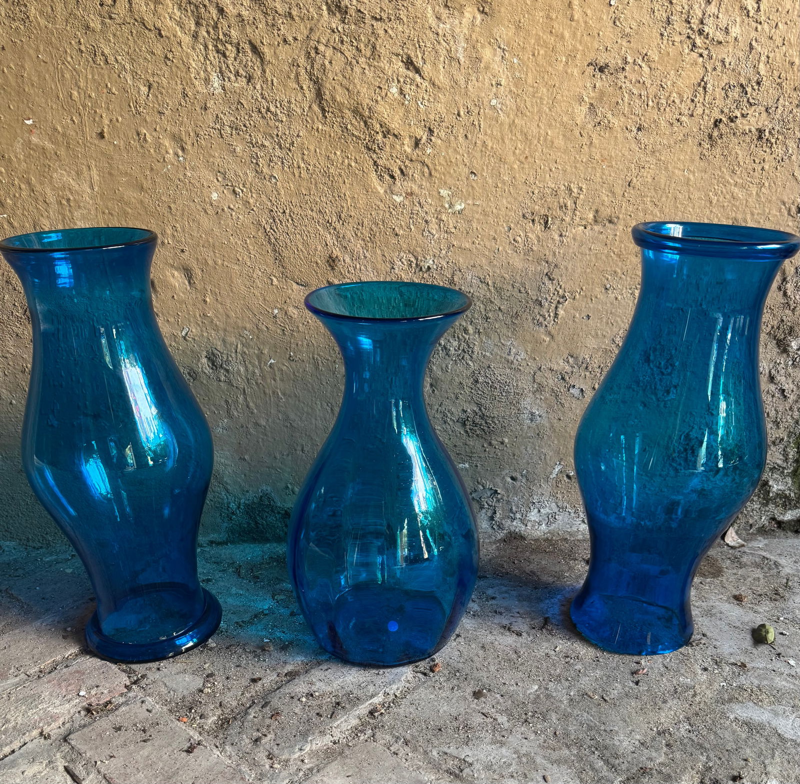 Pair of peacock blue glass hurricanes and matching oversized peacock blue glass vase: Pair of peacock blue glass hurricanes and matching oversized peacock blue glass vase. DIMENSIONS: Hurricanes- 6"D x 18"H Vase- 6"D x 16"H