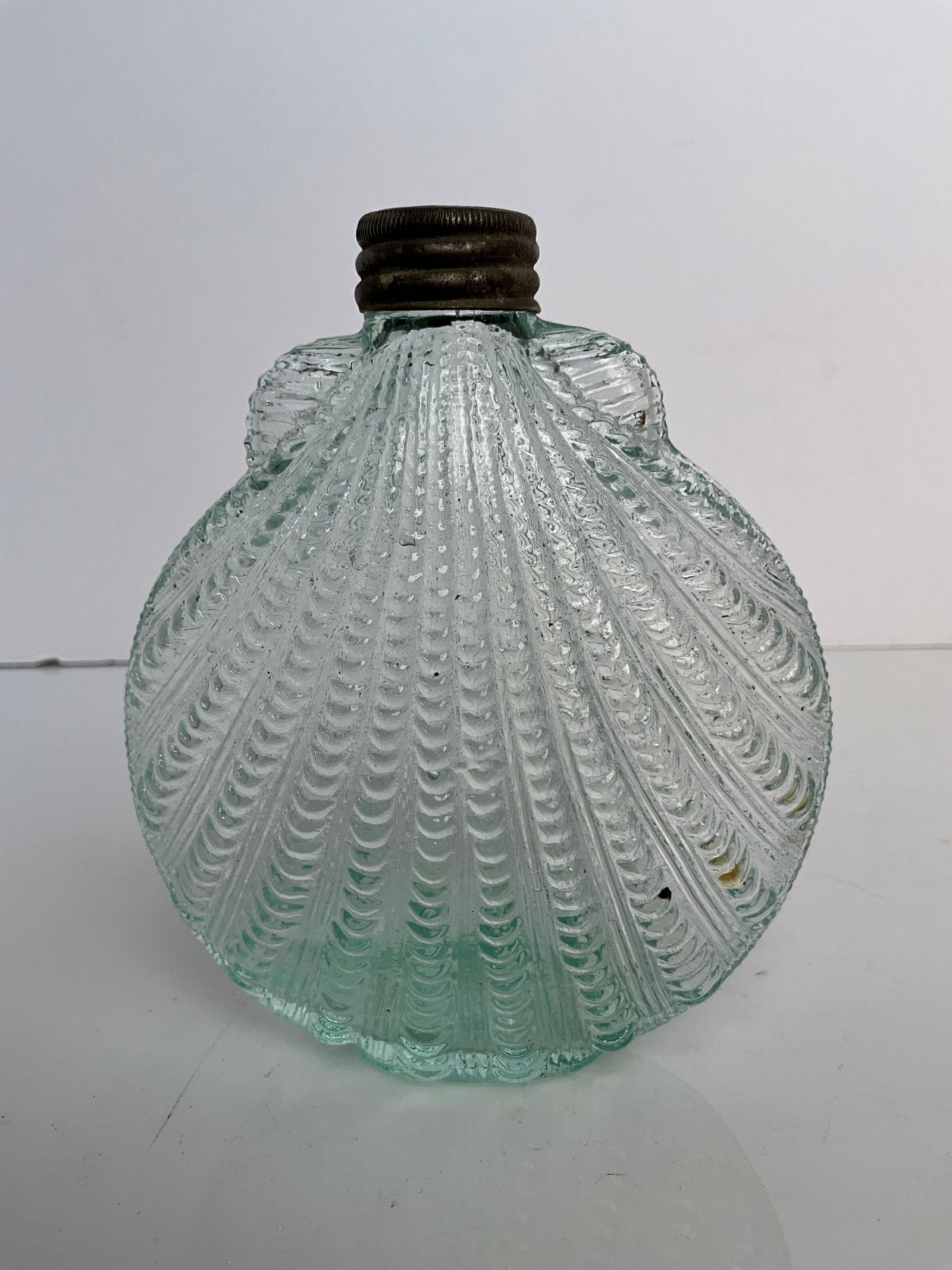 Early pocket flask in the shape of a shell: Early pocket flask in the shape of a shell, nice green aqua color. these hard to find pocket flasks are highly desirable smooth base with a ground lip original metal cap. There is a chip on the side o