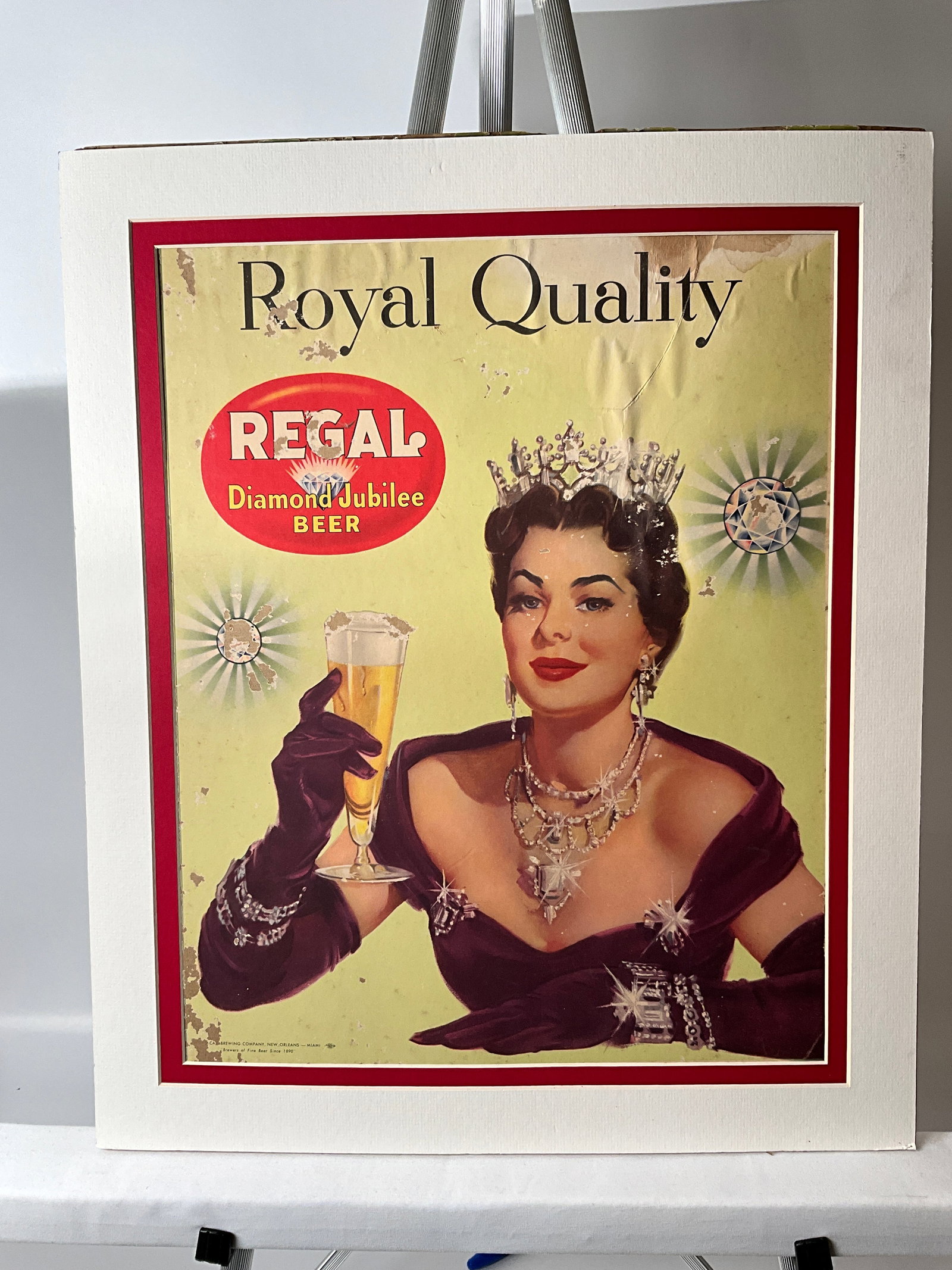Regal Diamond Jubilee Beer, New Orleans-Miami, Royal Quality Brewriana Advertising Sign: Beer advertising sign from Regal Diamond Jubilee Beer. Paper on cardboard. The matted frame appears to have been taped with double-sided tape to the image and will not be able to be removed easily. Th