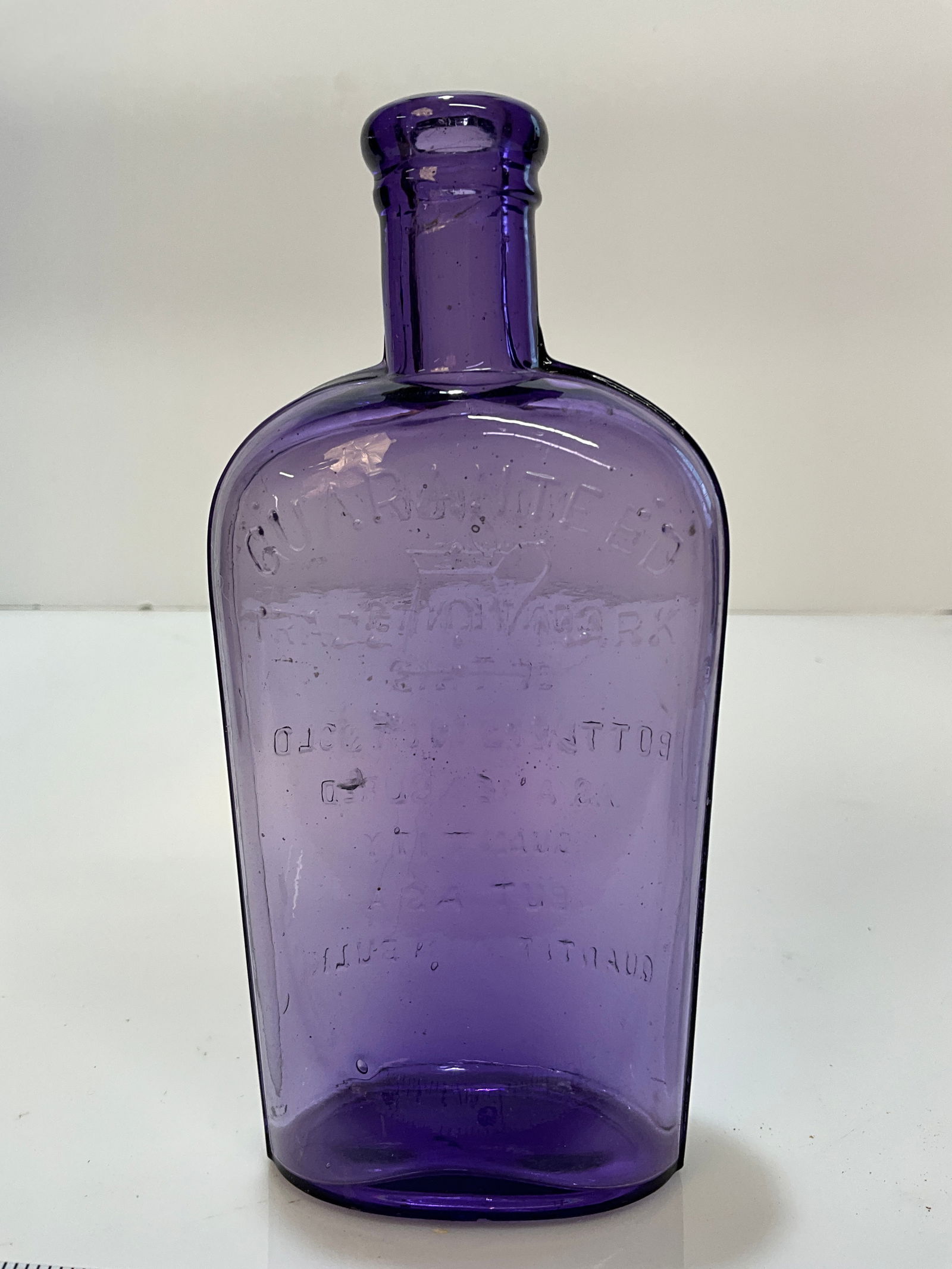 1/2 Pint Guaranteed, embossed Teapot Purple Flask: 1/2 Pint Guaranteed, with an embossed Teapot, Purple Flask. Lots of embossing on the reverse on the back of this Flask. Fleabite bruise on the reverse of the bottle in the middle of the embossing.