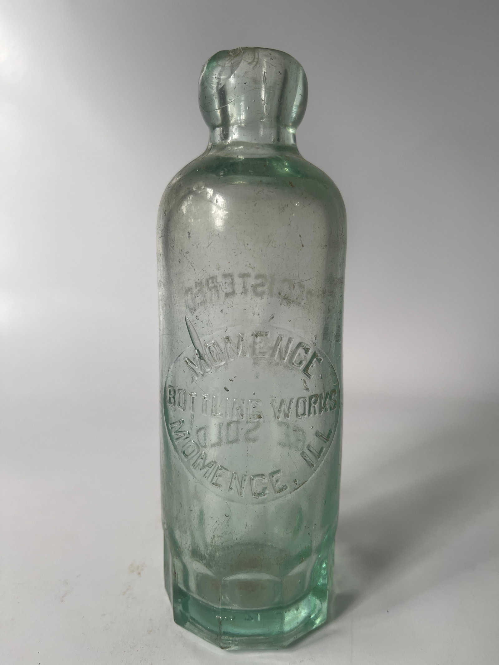 Momence Bottling Works Momence, Ill hutch soda: Here is a Momence Bottling Works Momence, Ill hutch soda. The bottle is aqua in color and has a mug base. There is a chip on the lip but no other damage.