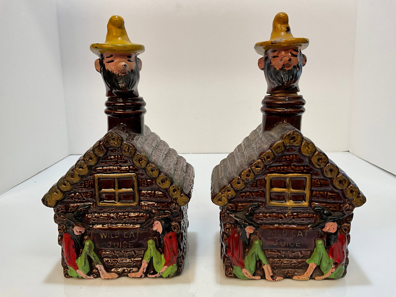 Lot of Two - Moonshine Whiskey "Wild Cat Juice" Log Cabins. with hillbilly's on the front: Lot of Two - Moonshine Whiskey "Wild Cat Juice" Log Cabins. with hillbilly's on the front and a Hillbilly's head as the stopper.