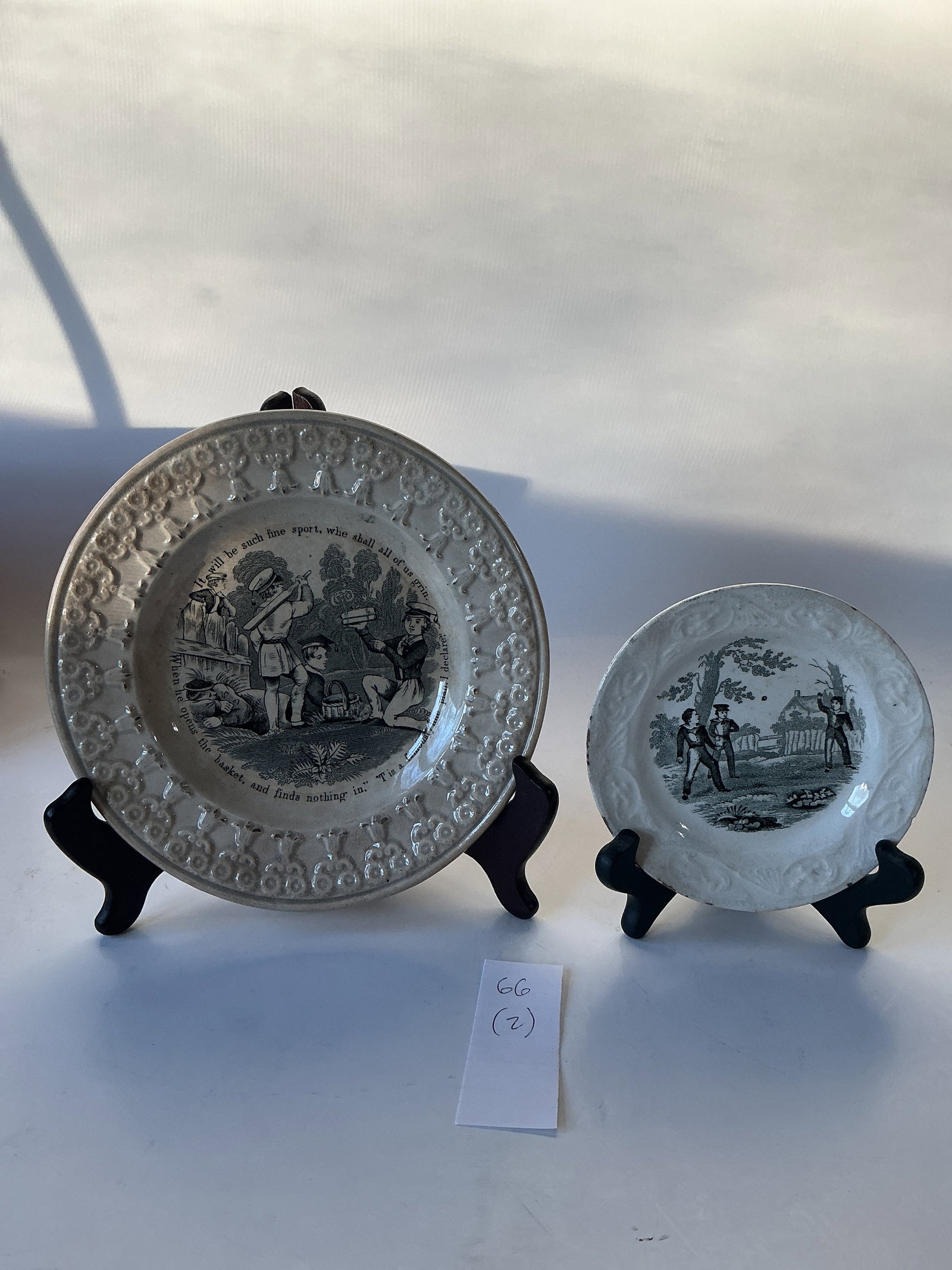 Two Plates With Boys Playing: The small 5" plate has three boys tossing a ball. The 7 3/4" plate has boys playing with a brick bat after school. Both have floral embossed borders. In fair condition. Both are darkened and the small