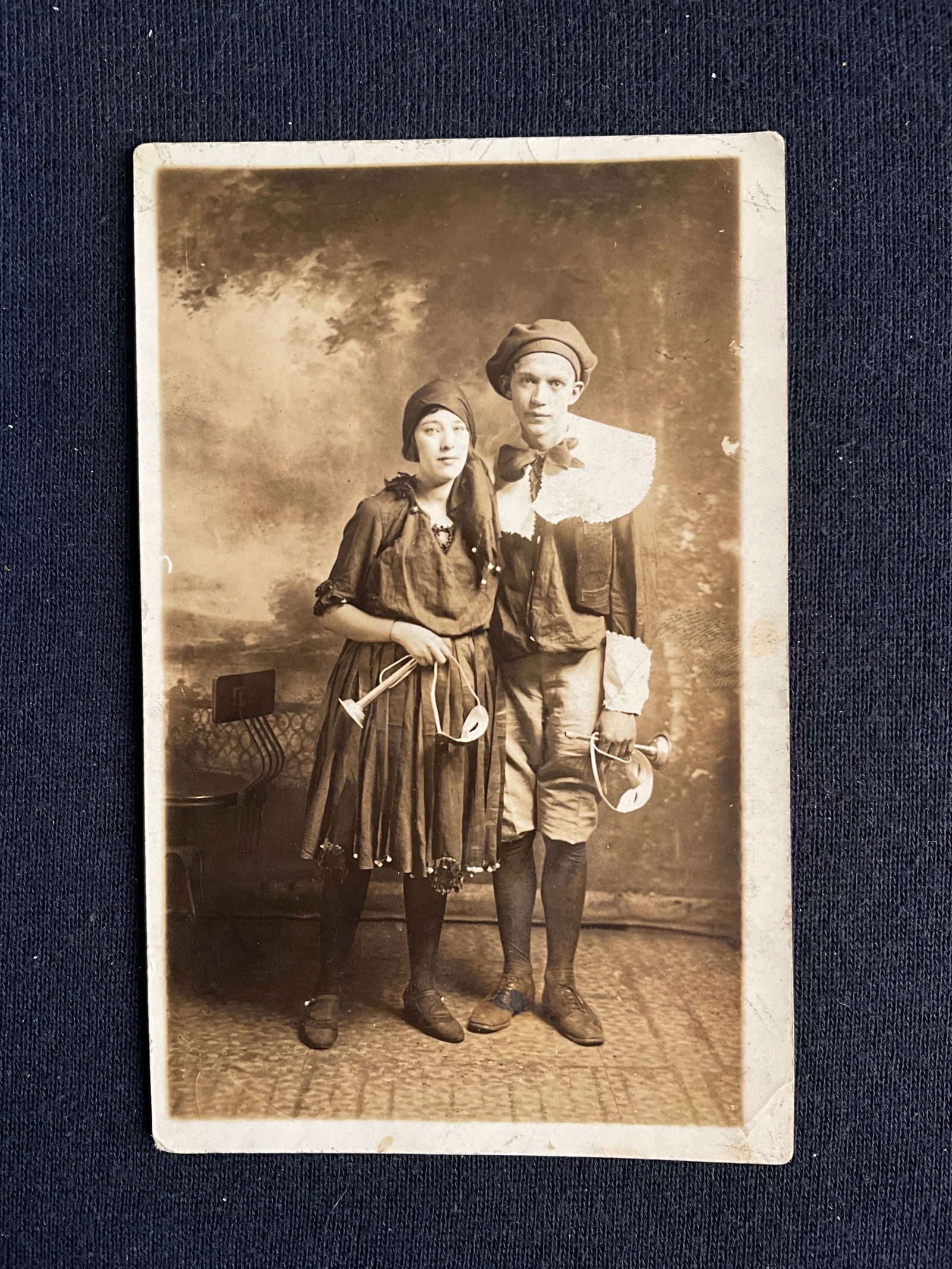 Post Cards, Ca. 1900s – Photo card, Halloween Post Cards - RARE: Unused photo card of an unidentified man & woman in a studio, holding masks and horns and possibly dressed for a Halloween party. Has 4 very minor crimps/creases & the reverse is discolored.