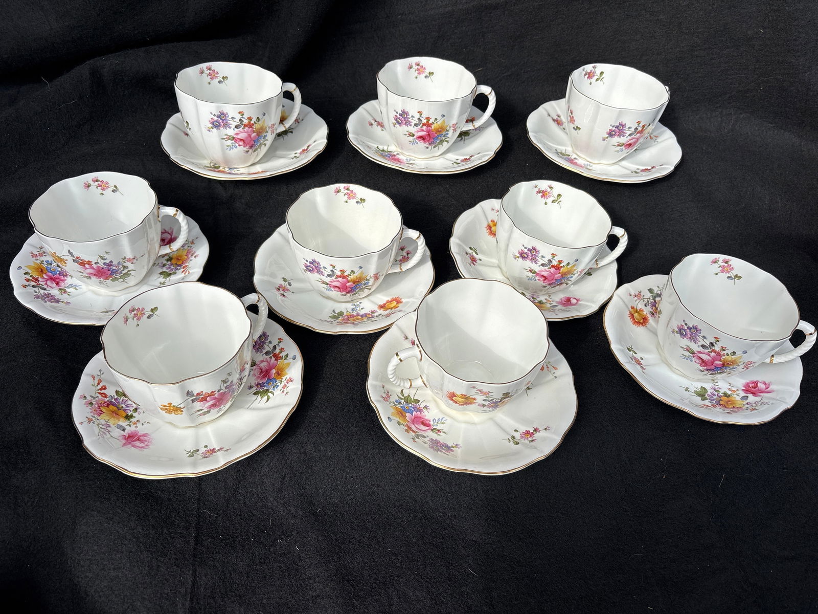 Mid century uncommon set of nine oversized breakfast Derby Posie pattern cups & saucers: Royal Crown Derby Derby Posies bone china cup with a fluted edge and gold trim. The pattern, "Derby Posies," features various small floral motifs. It was produced by Royal Crown Derby from 1900 throug