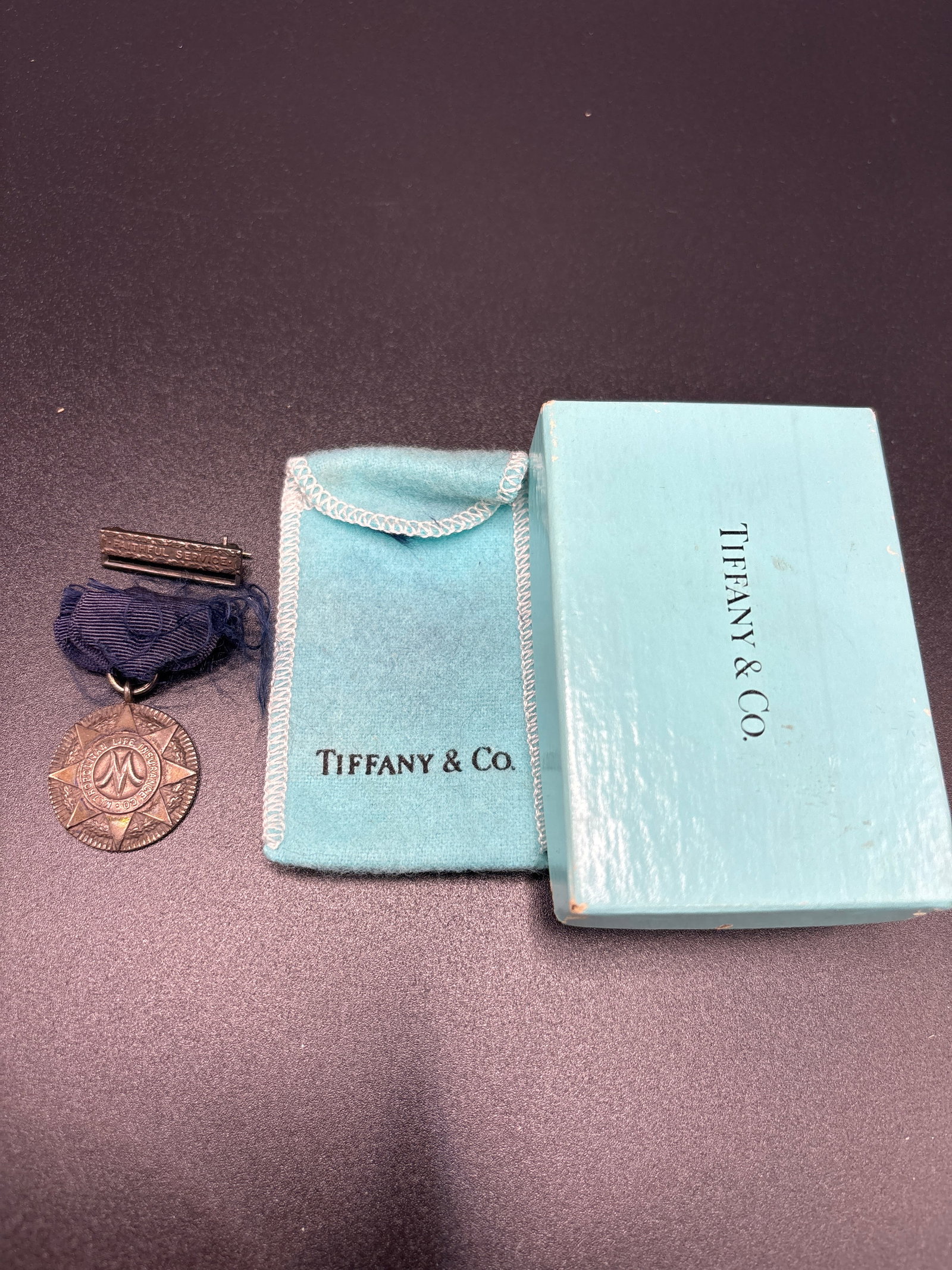 Vintage Tiffany & Co. sterling silver 1 inch medal Met Life Insurance w/pouch; 13.2 grams: Vintage Tiffany & Co. sterling silver 1 inch medal Metropolitan Life Insurance w/pouch; 13.2 grams inclusive of ribbon.Appears to be original Tiffany robins egg blue felt pouch and box.good condition 