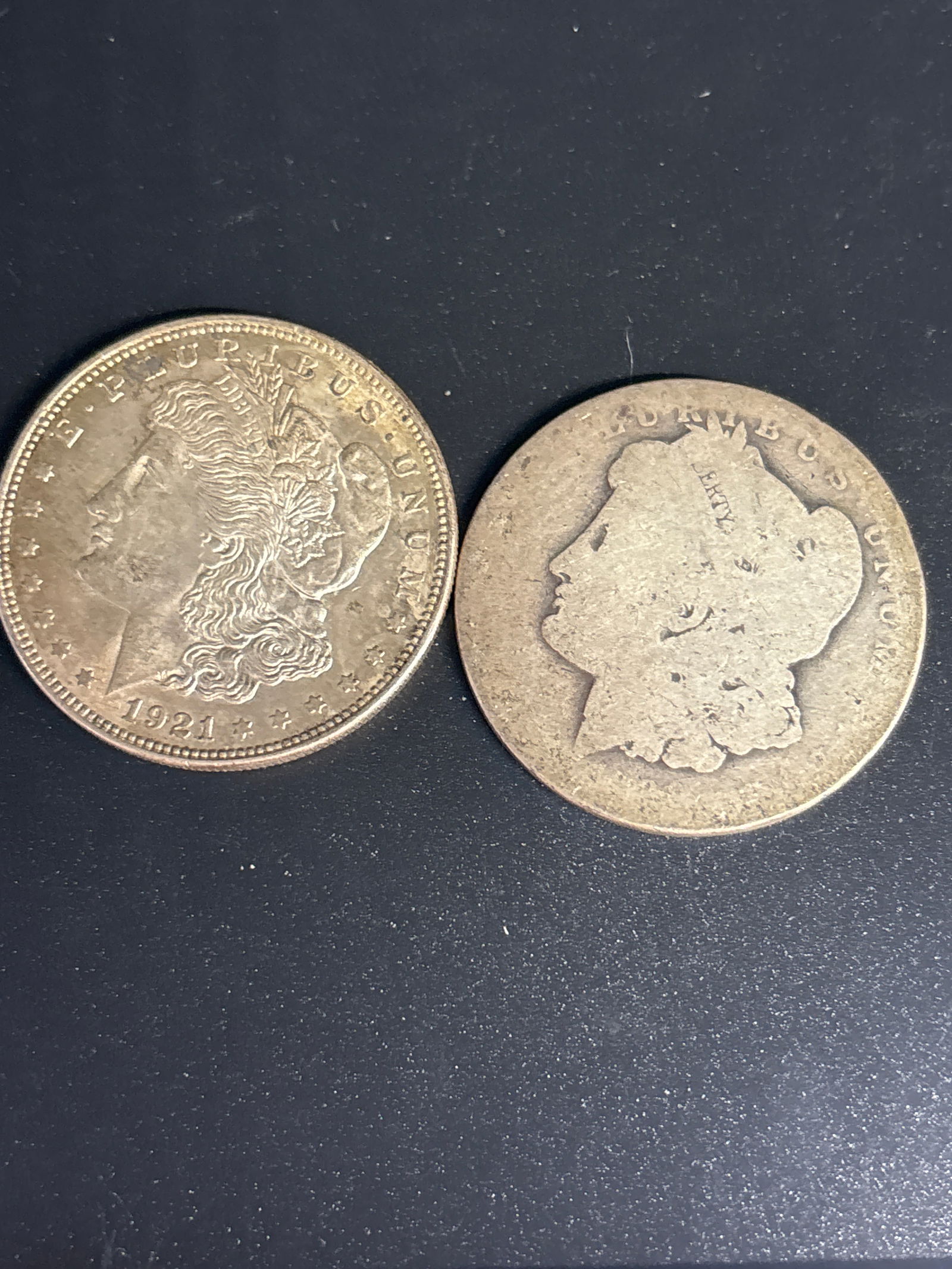 Two United States Morgan silver one dollar coins; one worn: 1921 Morgan Silver Dollar, which was the final year of production for this classic series, known as the "King of America's Coins". Composition: Contains 0.7734 troy ounces of 90% pure silver. Design: