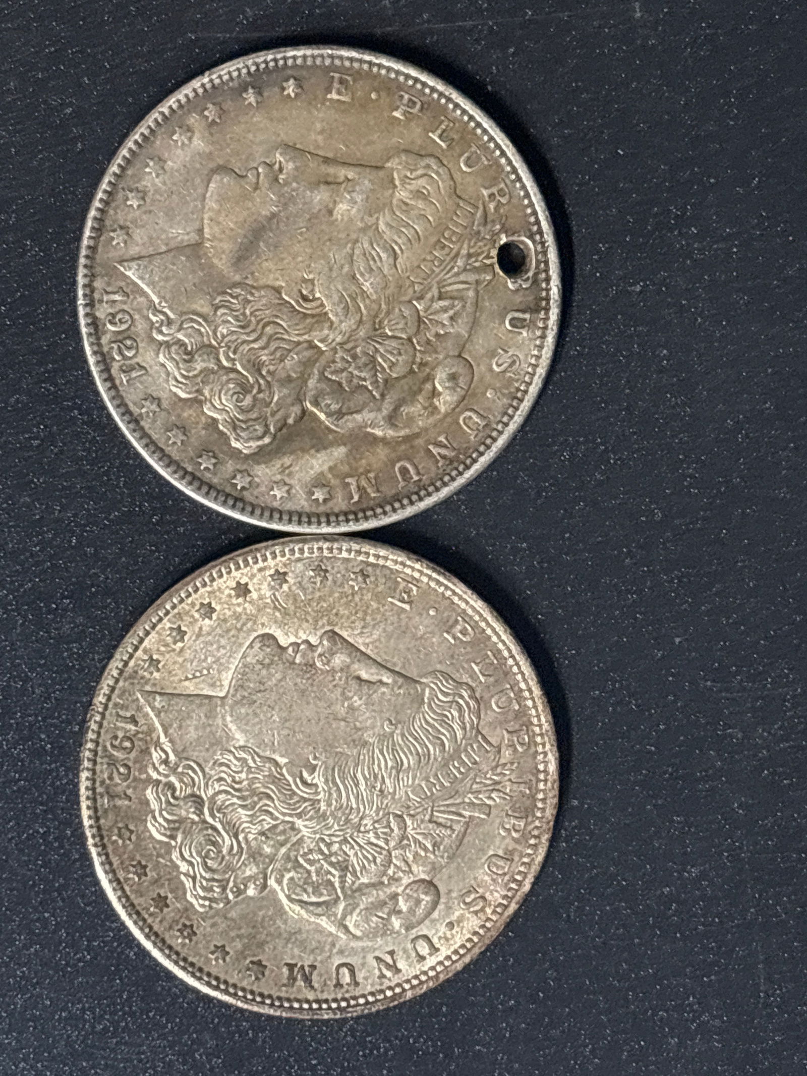Two 1921 Morgan United States Silver Dollars; one holed: Two 1921 Morgan Silver Dollars.Composition: These coins are typically composed of 90% silver and 10% copper, containing 0.77344 troy ounces of pure silver. Design: The obverse features Lady Liberty, a