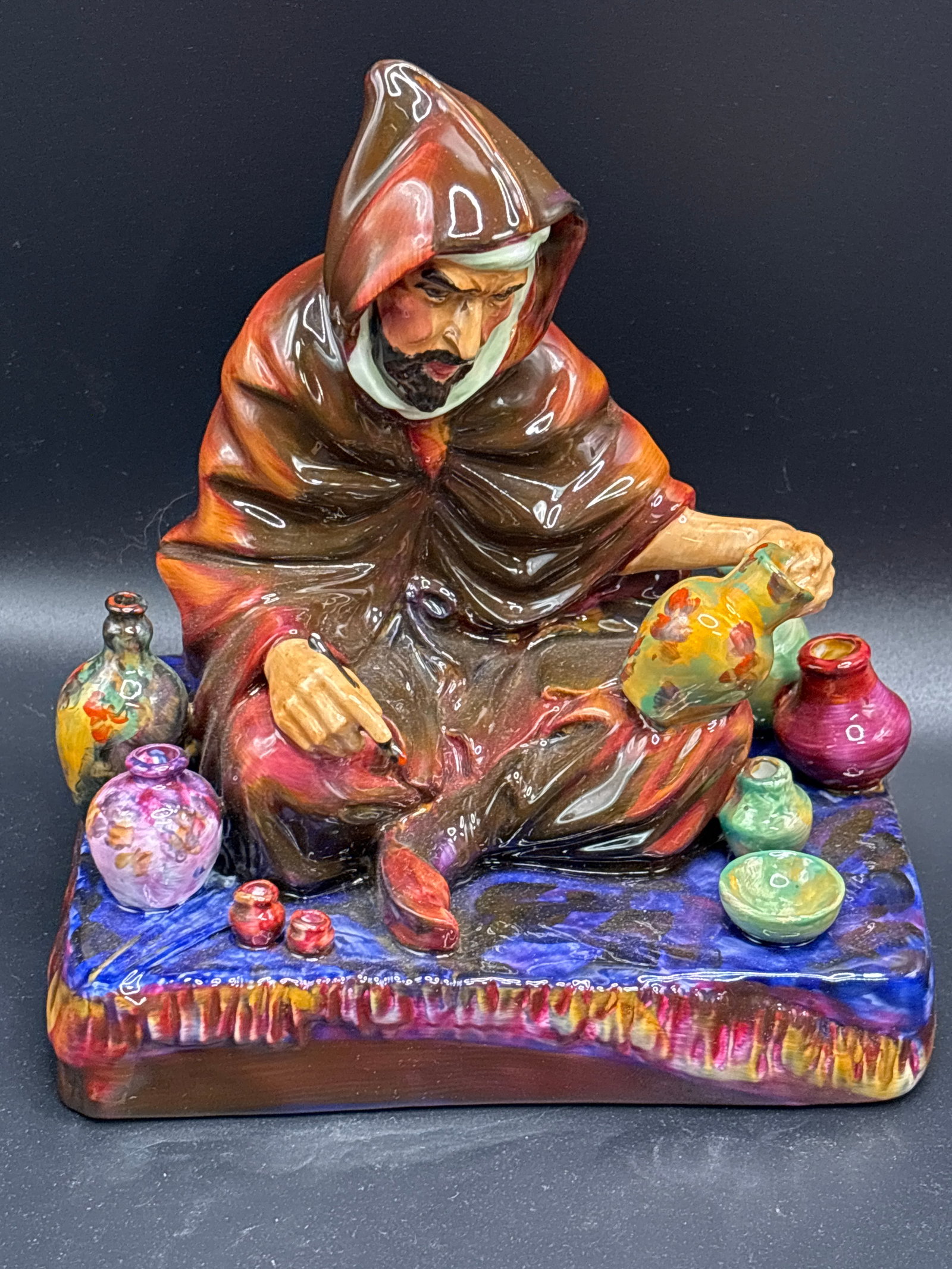 Retired Royal Doulton "The Potter" figurine, specifically model number HN 1493: Royal Doulton "The Potter" figurine, specifically model number HN 1493. Description: A hand-painted porcelain figurine depicting a robed figure seated on a textured base with various pots. Dimensions: