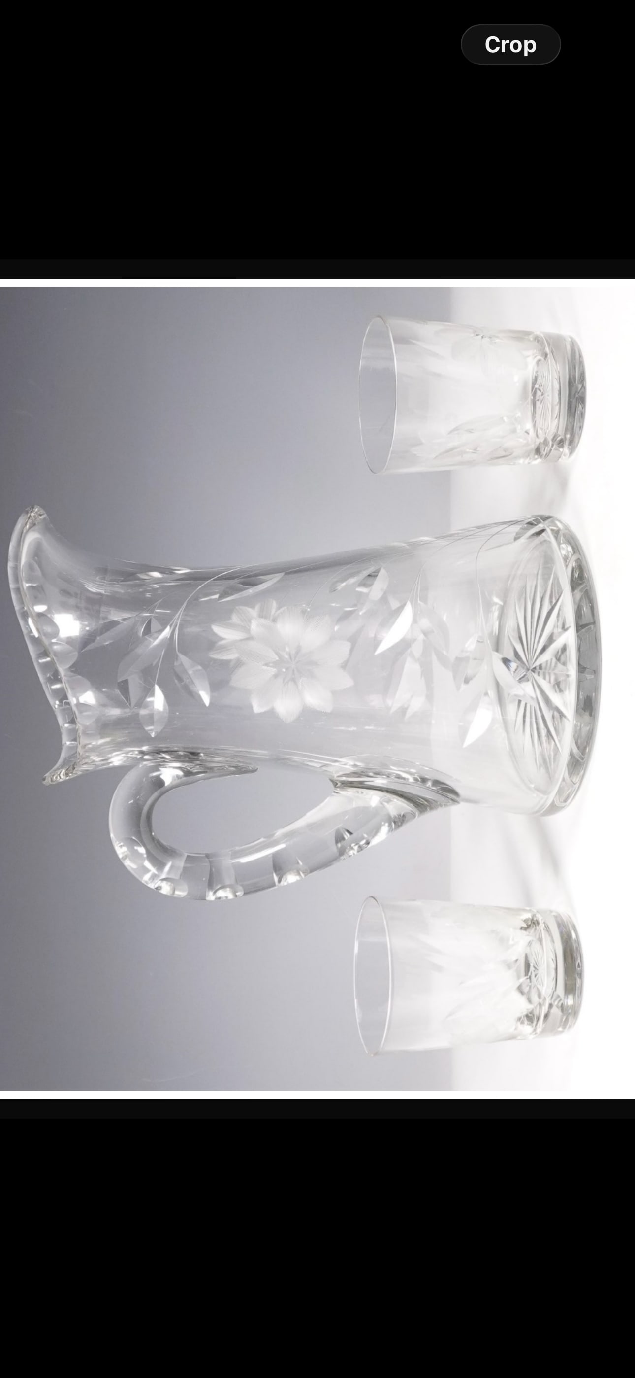 Antique Clear cut glass jug with two matching cups: Clear glass jug with two matching cups featuring etched floral decorations. The jug has a wide, curved spout and a sturdy handle with faceted detailing. The body is adorned with frosted floral motifs