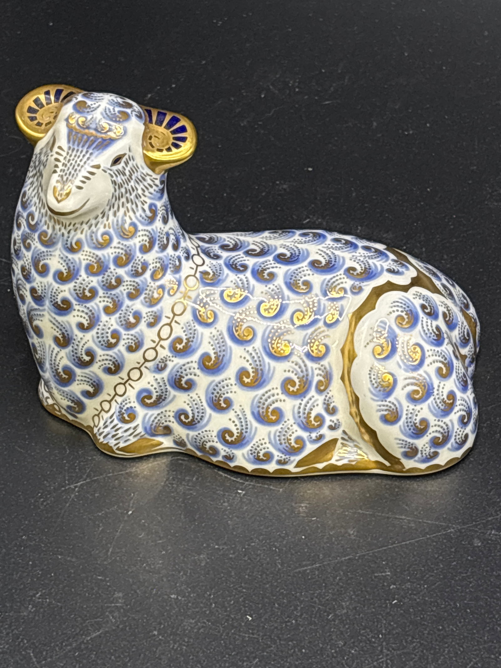 Big resting sheep Royal Crown Derby bone china 4&1/4 inch paperweight: First Quality. Gold stopper. No box. Royal Crown Derby paperweight designed as a resting sheep or ram with Imari-inspired blue and gold detailing.This piece was likely issued around 1992 and measures 