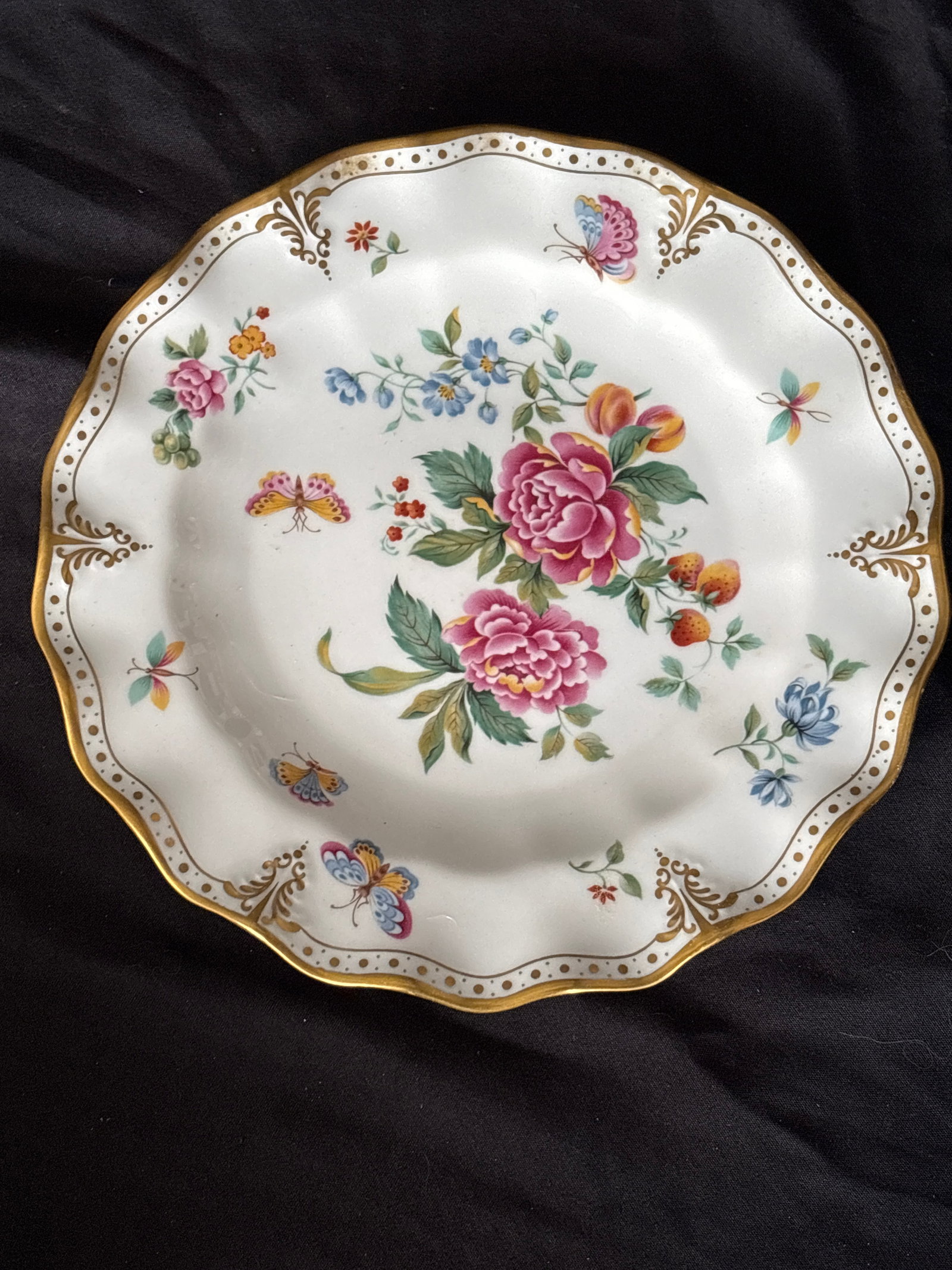 Wavy edge ‘Derby Days’ Royal Crown Derby 7&3/4 inch plate: Wavy edge Royal Crown Derby dinner plate in the discontinued Derby Days pattern.Design Details: The plate features a floral and fruit design with butterflies, all adorned with a 22-karat gold gilded s