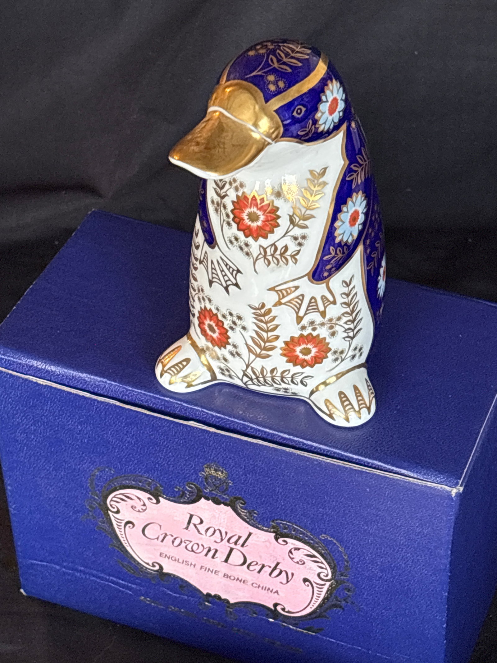 Royal Crown Derby Imari patterned platypus 4&3/4 inch paperweight: First quality. Gold stopper. With box. Royal Crown Derby Imari patterned platypus paperweight featuring intricate blue, white, and red floral designs with gilt detailing. These collectible figurines w