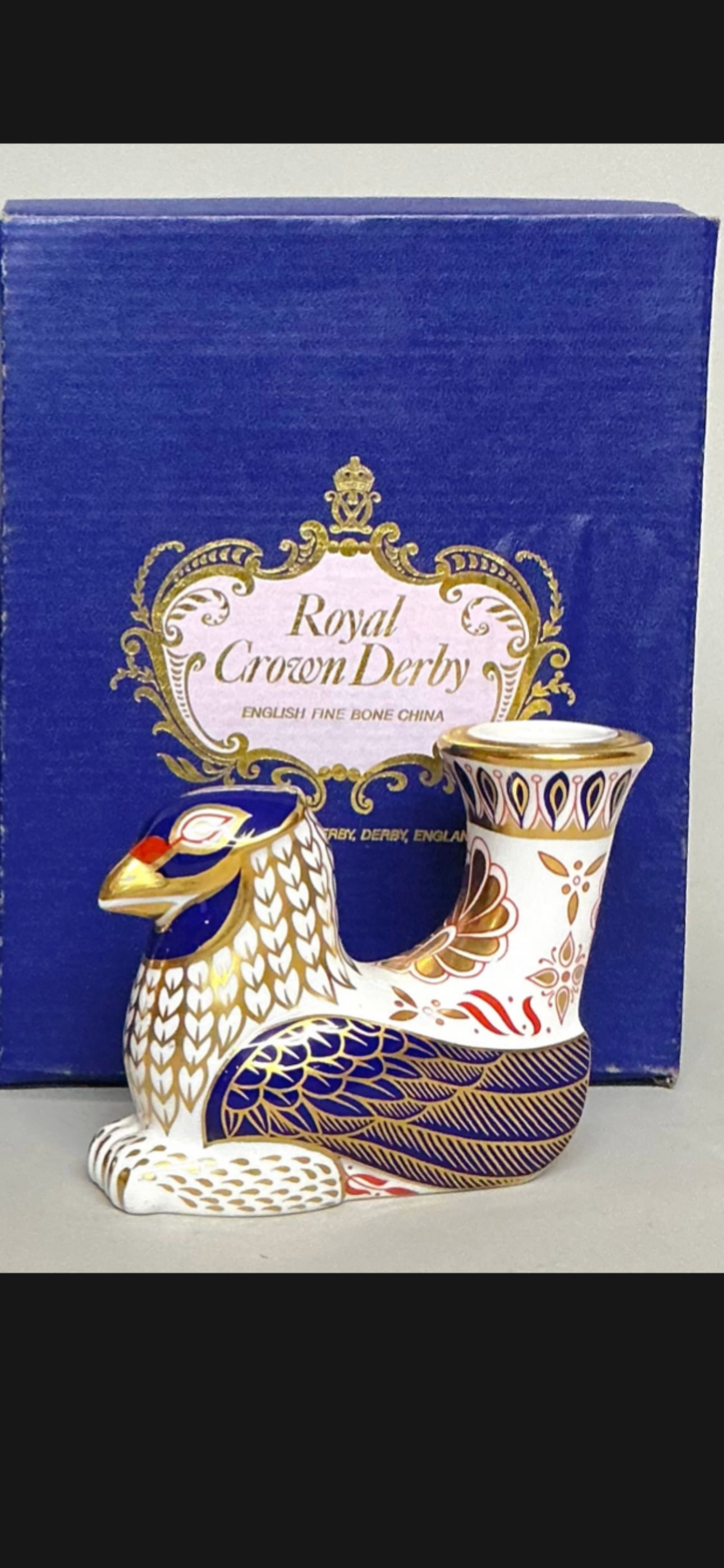 candle/paperweight Royal Crown Derby Griffin figurine from Mythical Beasts Series: Royal Crown Derby Griffin Mythical Beasts Bone China Candle Holder. It is crafted from fine bone china and decorated with 22-carat gold and intricate blue and red patterns.The design is part of a seri