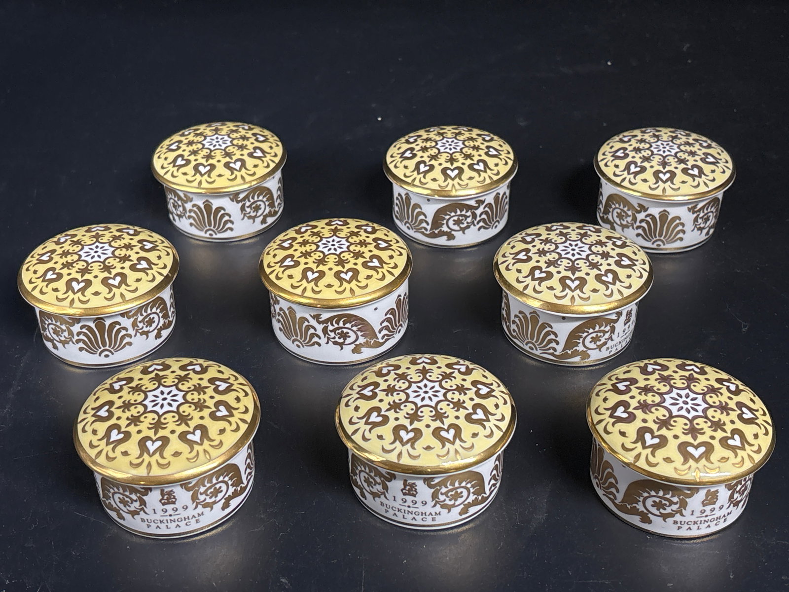 Set of nine collectible 1999 Buckingham Palace trinket boxes: Set of nine collectible 1999 Buckingham Palace trinket boxes featuring a damask pattern and gold accents, made of fine bone china. Design: White drawing room design inspired by Buckingham Palace. Mate