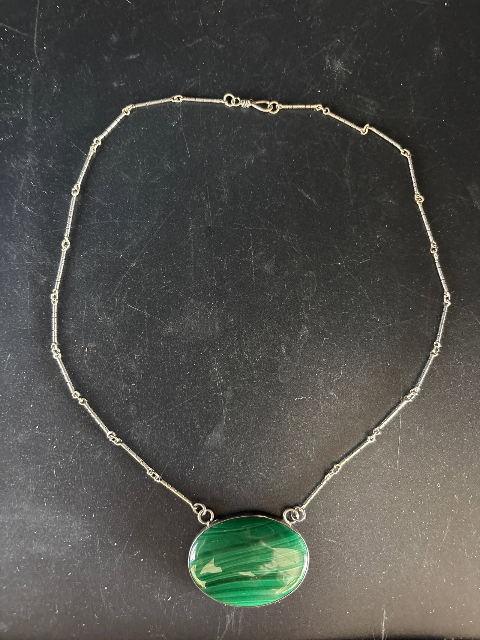 sterling silver necklace featuring a banded green malachite oval gemstone pendant: sterling silver necklace featuring a banded green malachite oval gemstone pendant.Materials: The pendant setting and chain are made of 925 sterling silver.Design: The piece consists of a polished oval