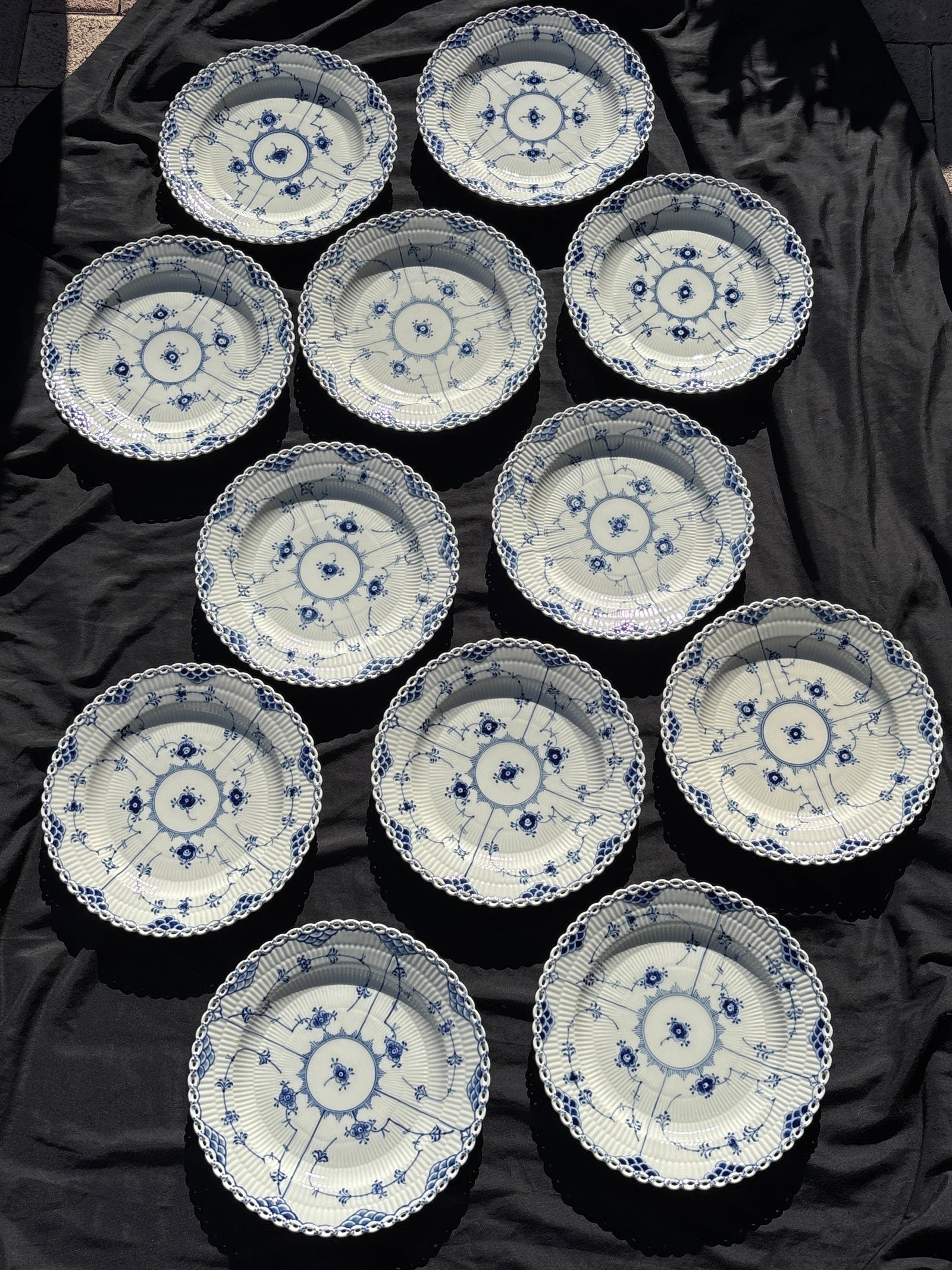Twelve Royal Copenhagen "Blue Fluted Full Lace" 9&7/8 inch plates (Model 1084): featuring a hand-painted floral motif.Intricate Border: The plate is known for its open-work lace border, where each small hole is meticulously crafted by hand.Historical Pattern: Originally introduce