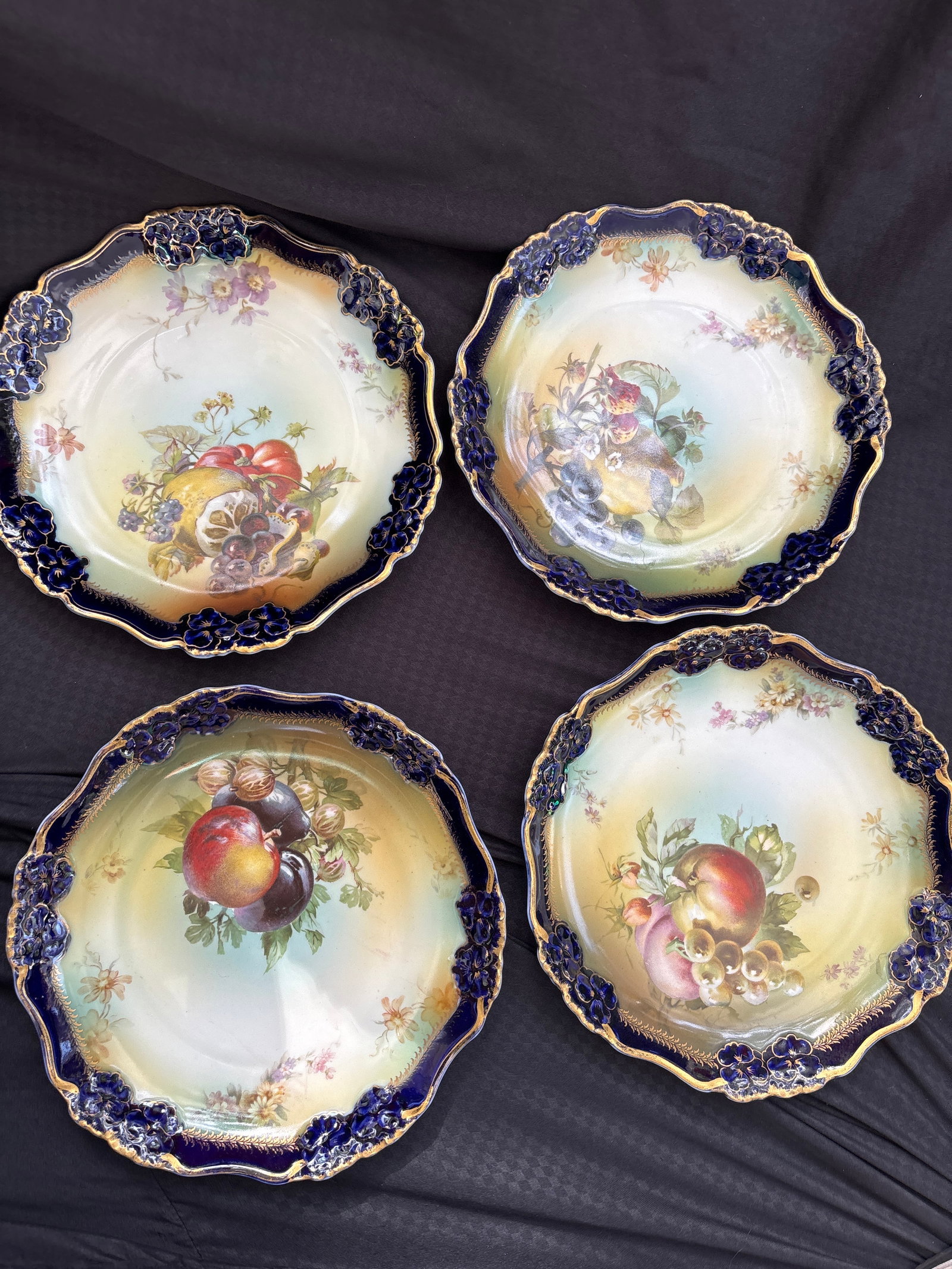 Antique set of four Bavaria porcelain 9 inch dishes: Antique set of four Bavaria porcelain dishes, likely from the early 20th century, featuring hand-painted fruit motifs and cobalt blue scalloped edges with gold trim.Manufacturer: The items appear to b