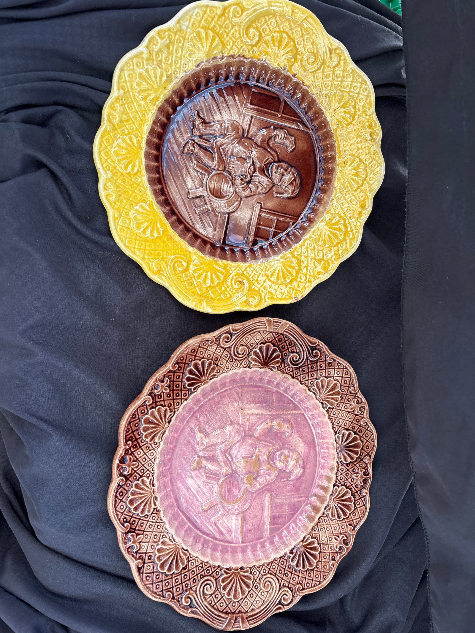 Two antique Majolica 10&1/2 inch platters relief design of a monk in a wine cellar: Two Antique Victorian Majolica Plates, likely dating back to the late 1880s.This specific pattern is often called the "Toby Man" or "Beer Drinking Man" scene. It features a central relief of a man in 