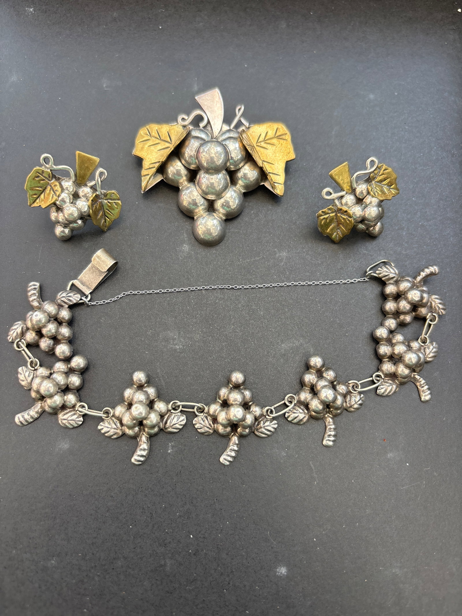 Four piece vintage Taxco Mexico sterling silver and brass grape leaf set; 44 grams: Four piece vintage Taxco Mexico sterling silver and brass grape leaf brooch pendant, earrings & bracelet. Materials: Constructed from 925 sterling silver with brass accents for the leaves.Design: Feat