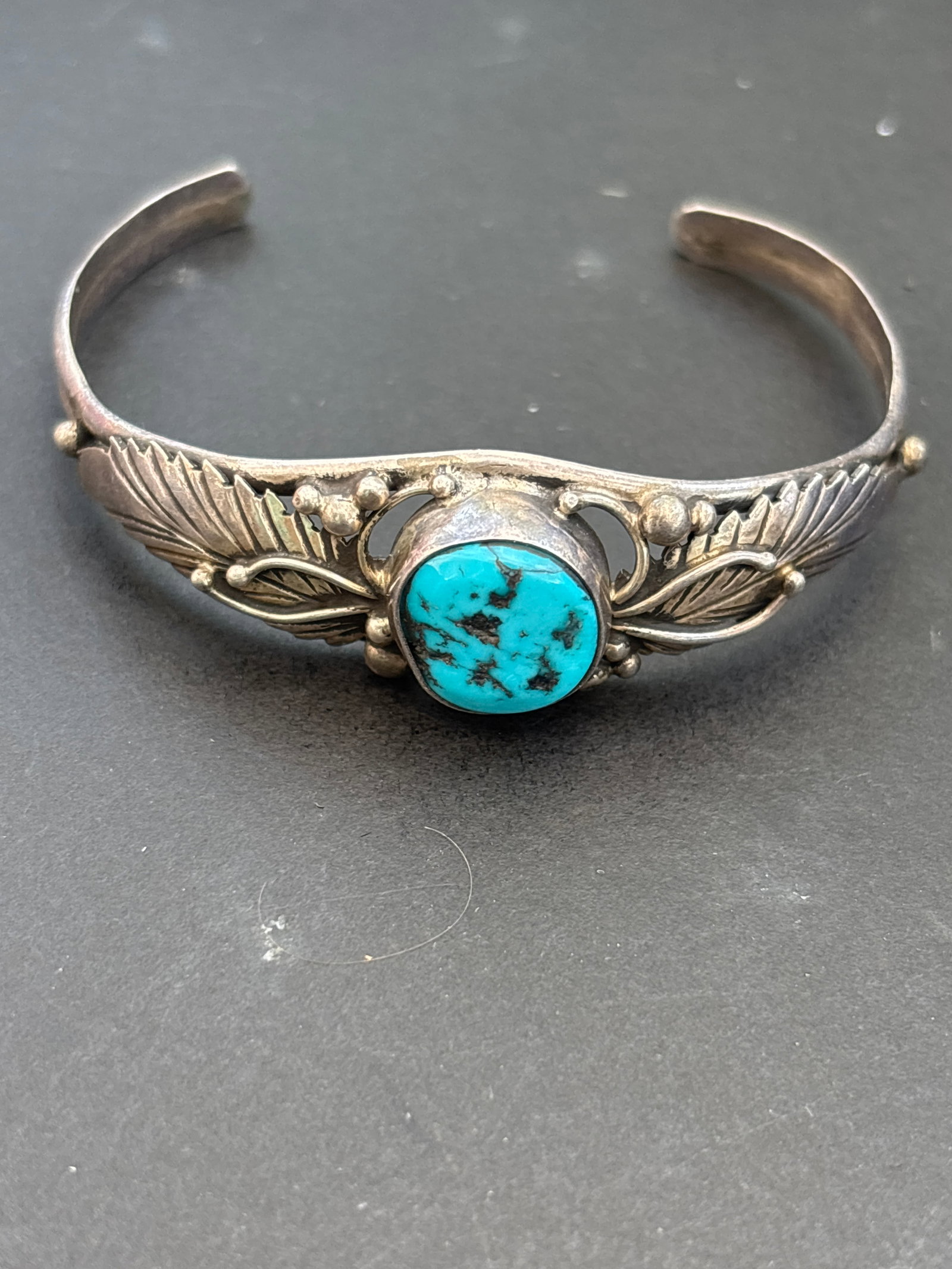 Small Navajo turquoise & Sterling Silver Cuff Bracelet; 13 grams: Small Navajo Sterling Silver Cuff Bracelet featuring a central turquoise cabochon. This style is a classic example of Native American jewelry, often characterized by handcrafted leaf or feather motifs