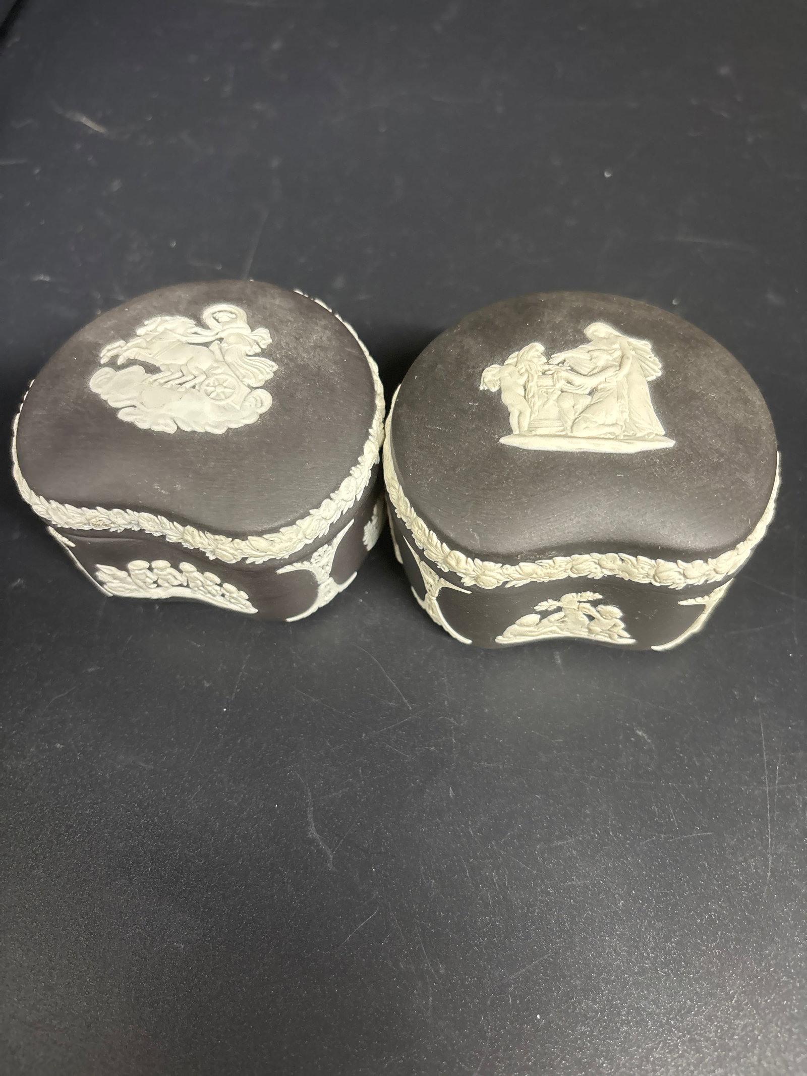 Two 3 inch vintage Wedgwood black basalt jasperware kidney-shaped trinket boxes: Two 3 inch vintage Wedgwood black basalt jasperware kidney-shaped trinket boxes. It features white relief figures in a classical or neoclassical style.The lid displays a scene of mythological figures,