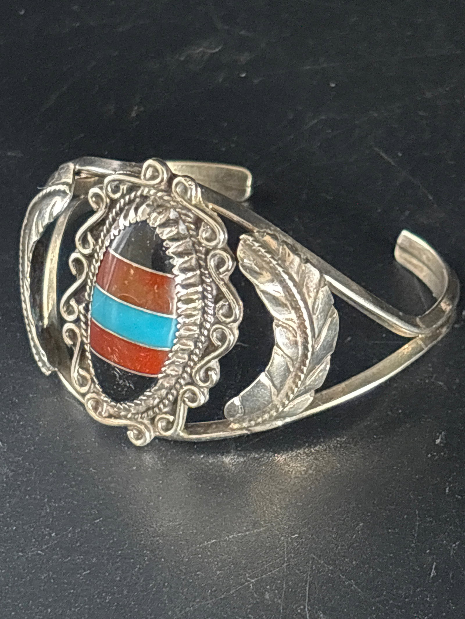 21 grams Sterling Navajo coral & turquoise inlay cuff bracelet: Navajo-style sterling silver cuff bracelet featuring coral and turquoise inlay.It has an intricate feather design on the sides of the cuff.The centerpiece is likely genuine red coral and turquoise